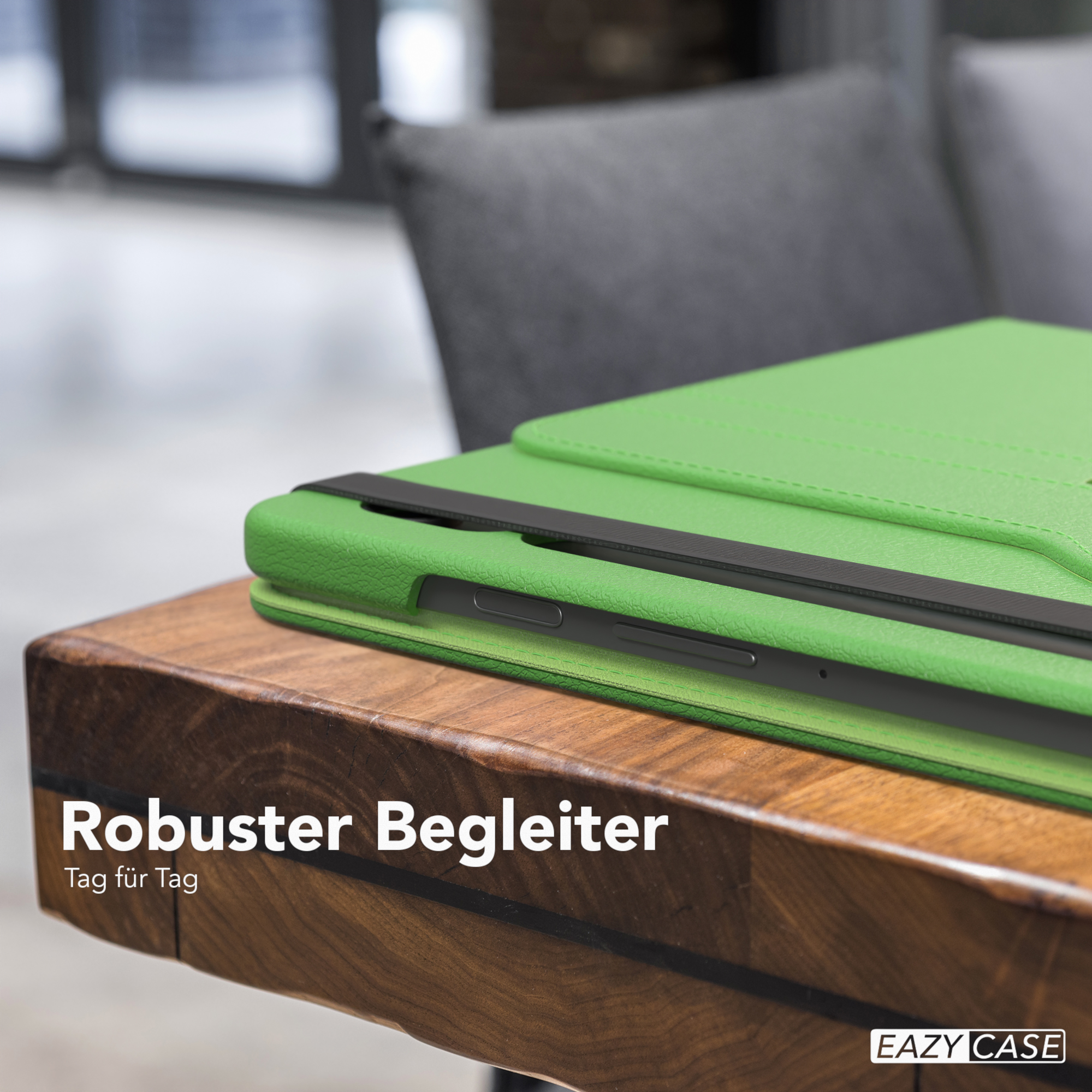 Grüne Tablethülle auf Holztisch. Schwarzes Band. Grauer Stuhl im Hintergrund.