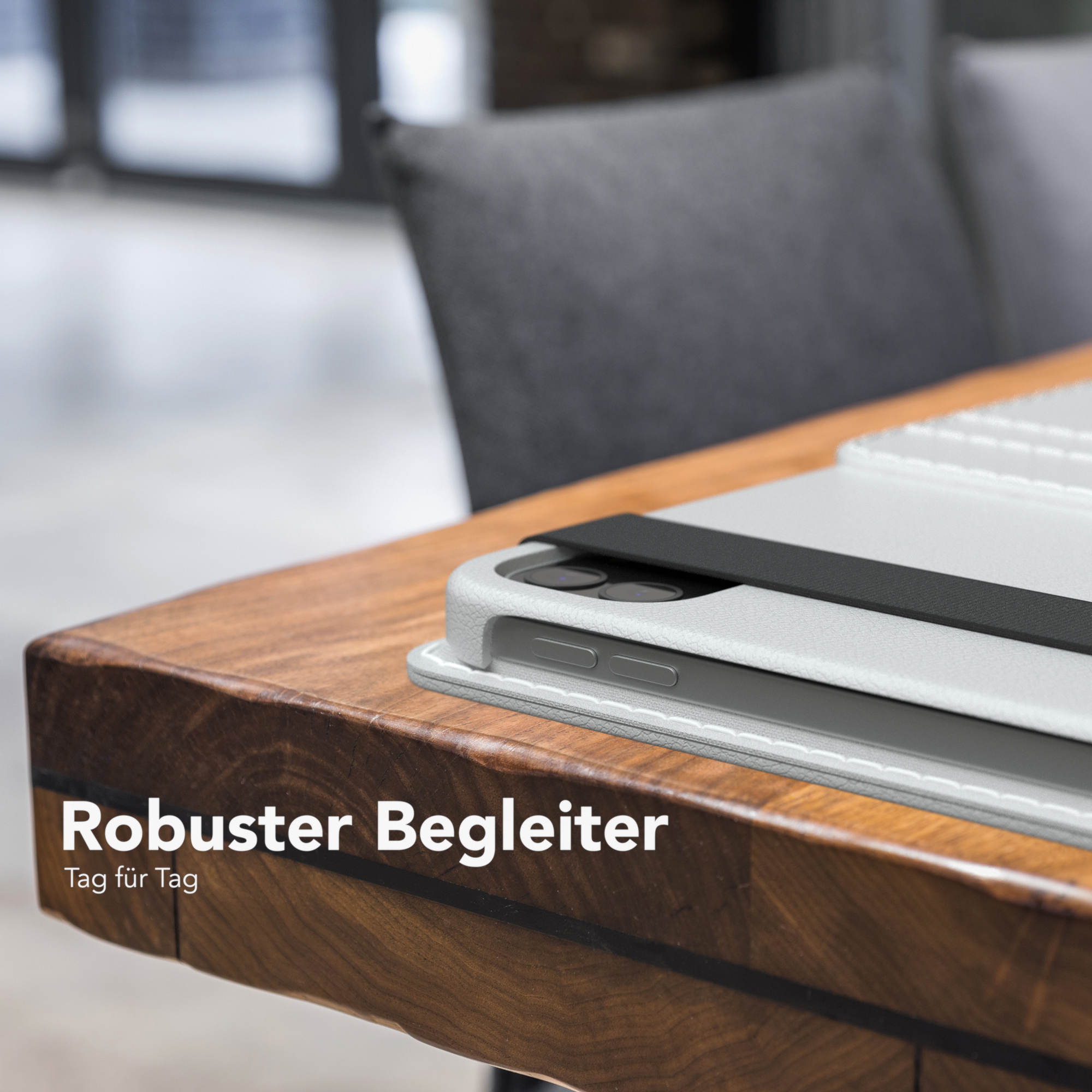Ein Tisch mit einer weißen Tablet-Hülle. Ein Stuhl ist im Hintergrund. Text: 'Robuster Begleiter'.