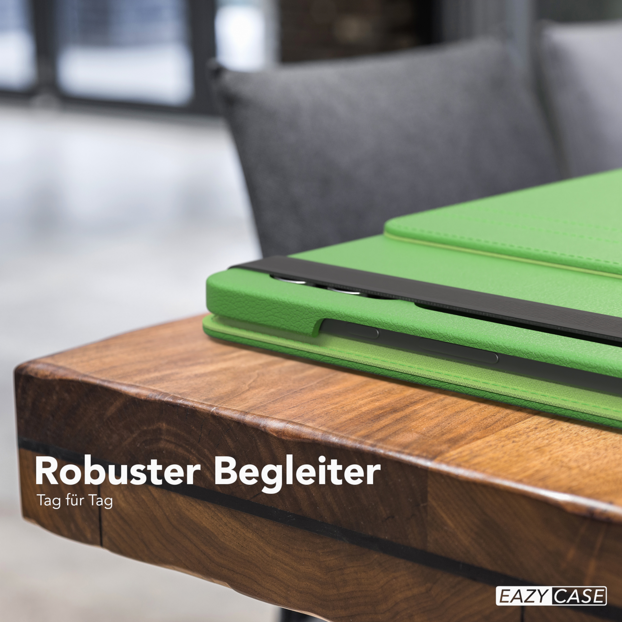 Grüne Tablet-Hülle auf einem Holztisch. Schwarzer Riemen. Grauer Stuhl im Hintergrund.