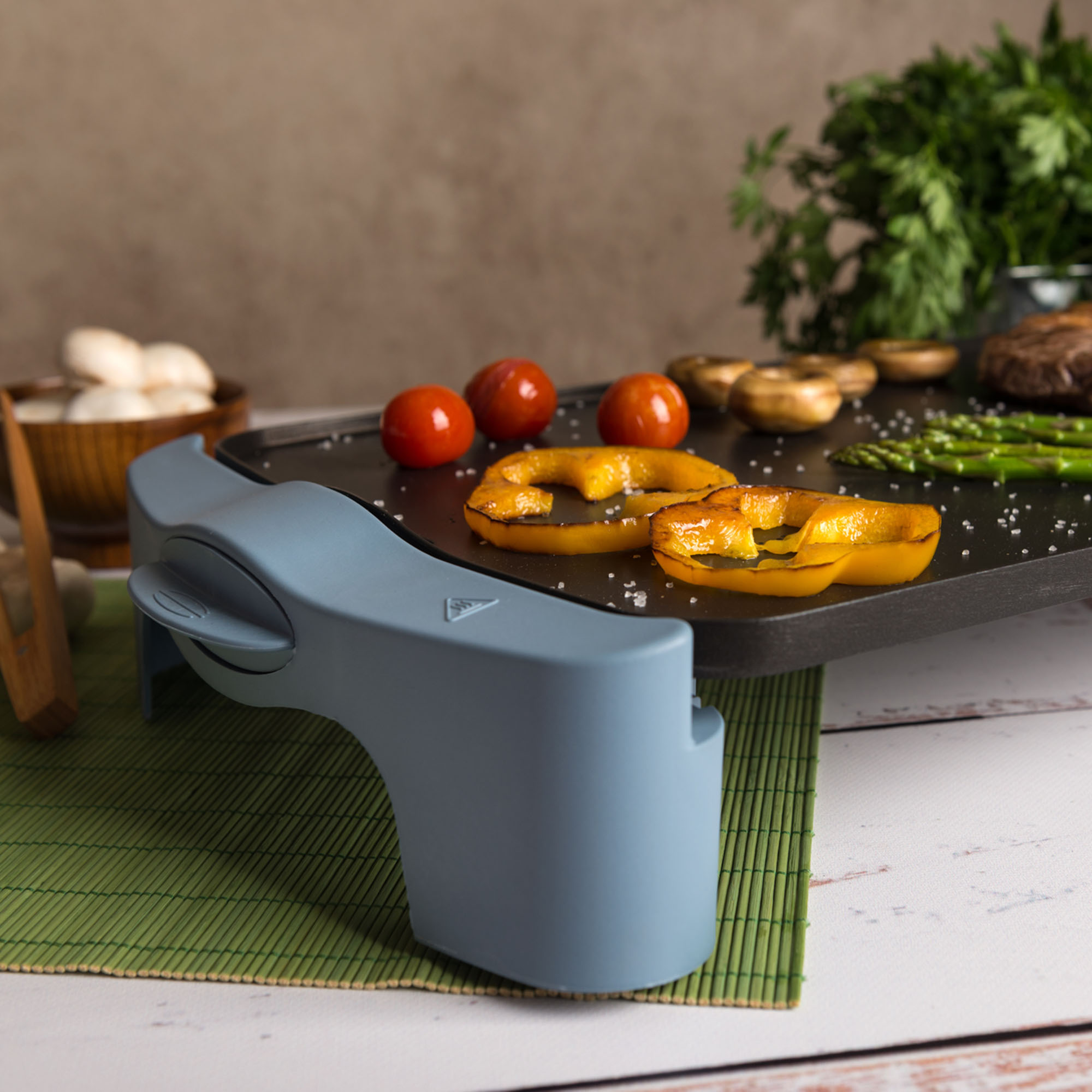 Una parrilla con tomates, pimientos y champiñones. Un asa azul en primer plano.