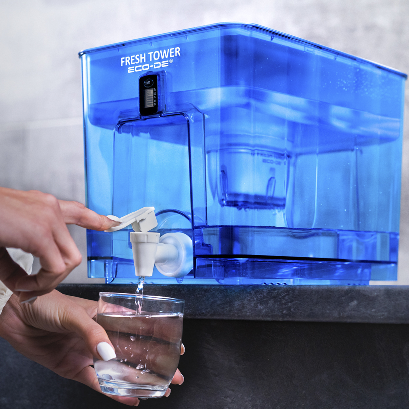 Dispensador de filtro de agua azul. Mujer usándolo para llenar un vaso con agua. Grifo blanco.