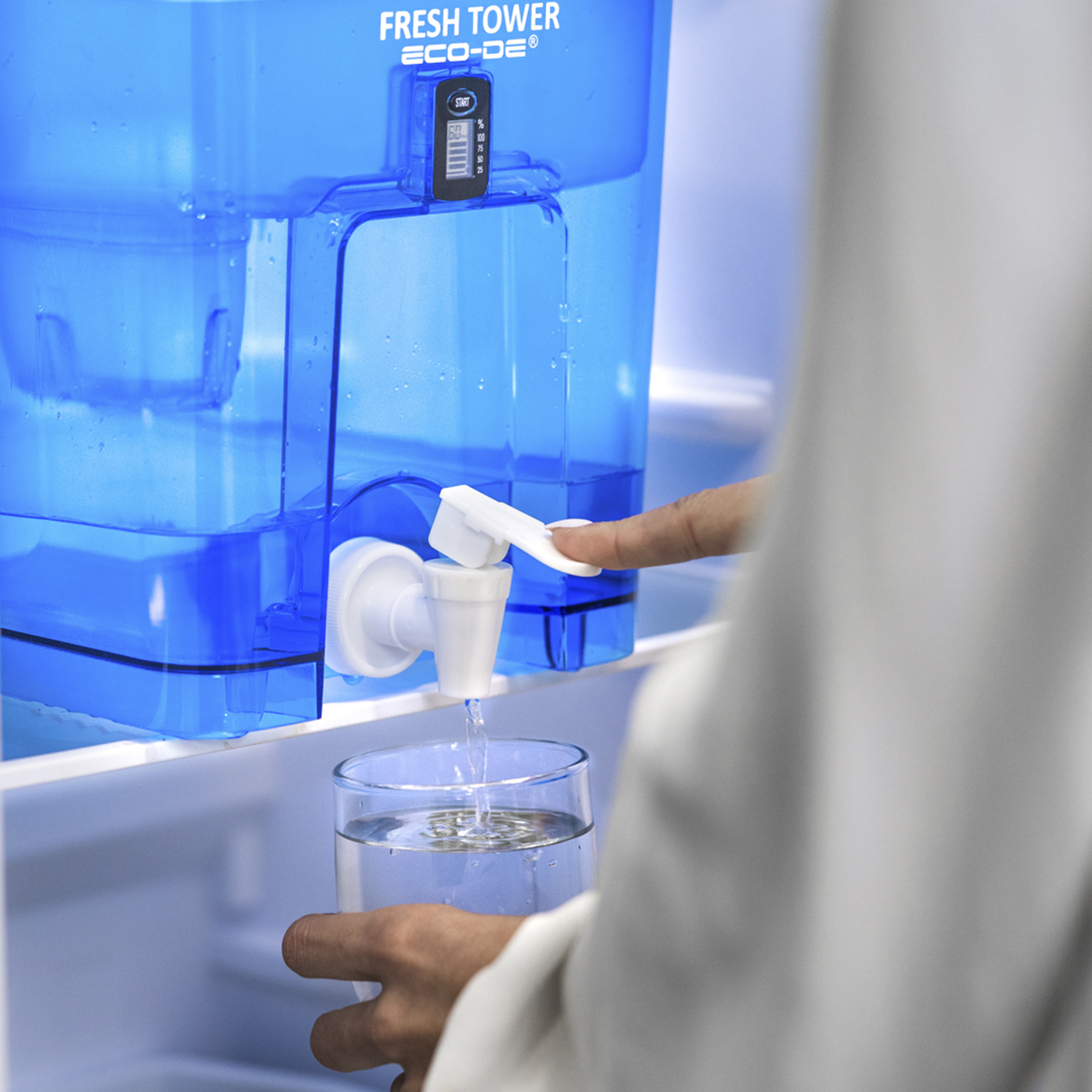 Una persona llenando un vaso con agua de un sistema de filtro de agua azul en un refrigerador.
