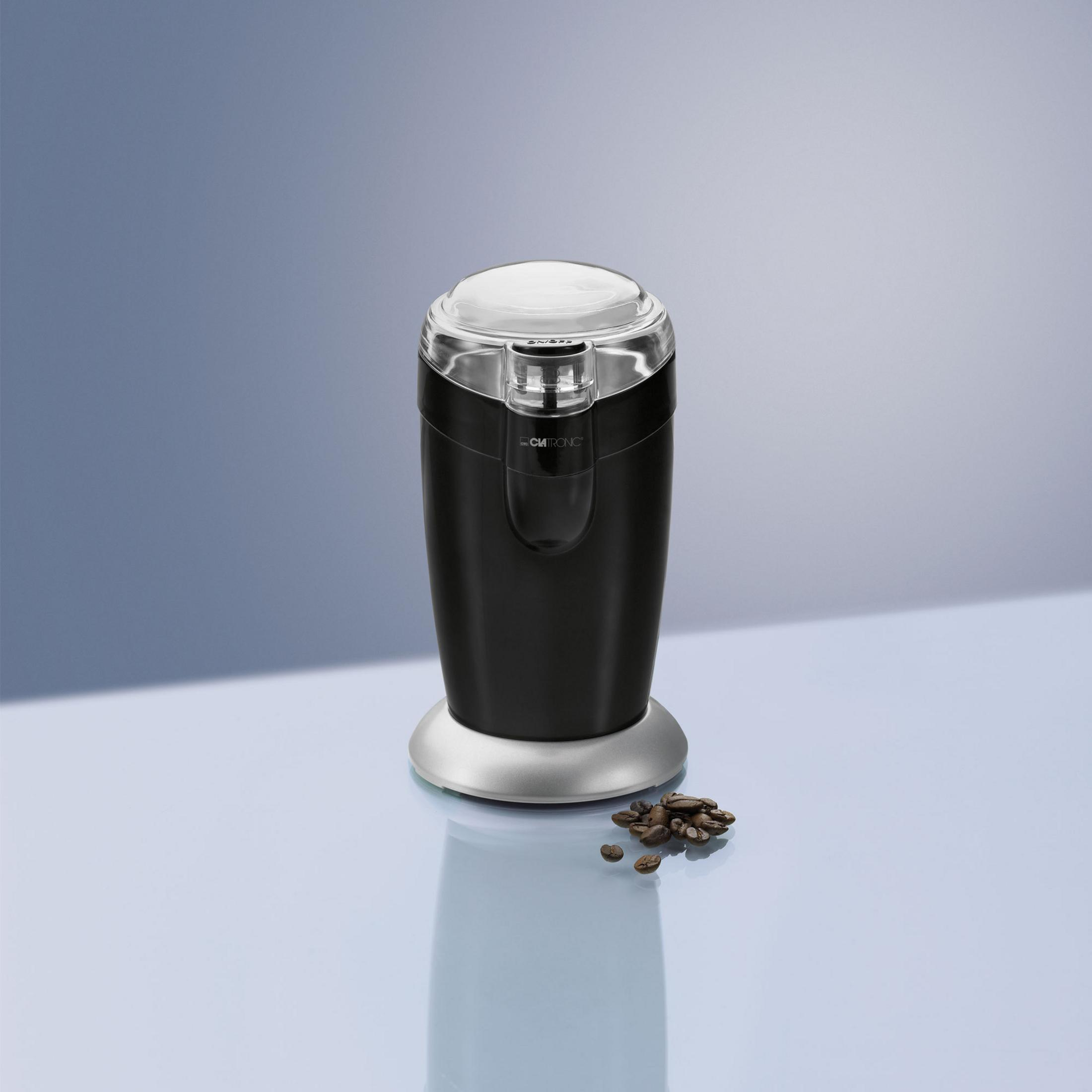 Czarny i srebrny młynek do kawy. Ziarna kawy na pierwszym planie. Niebieskie i szare tło.