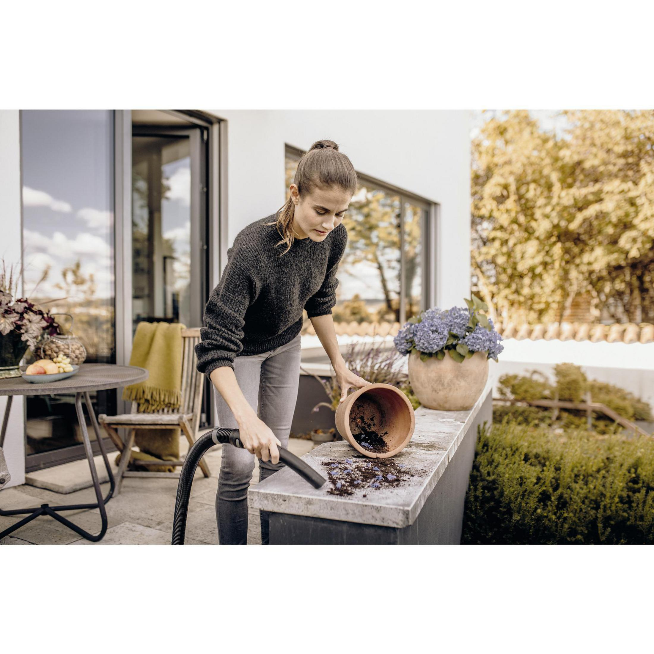 Kobieta czyszcząca donicę na patio odkurzaczem, otoczenie zewnętrzne.