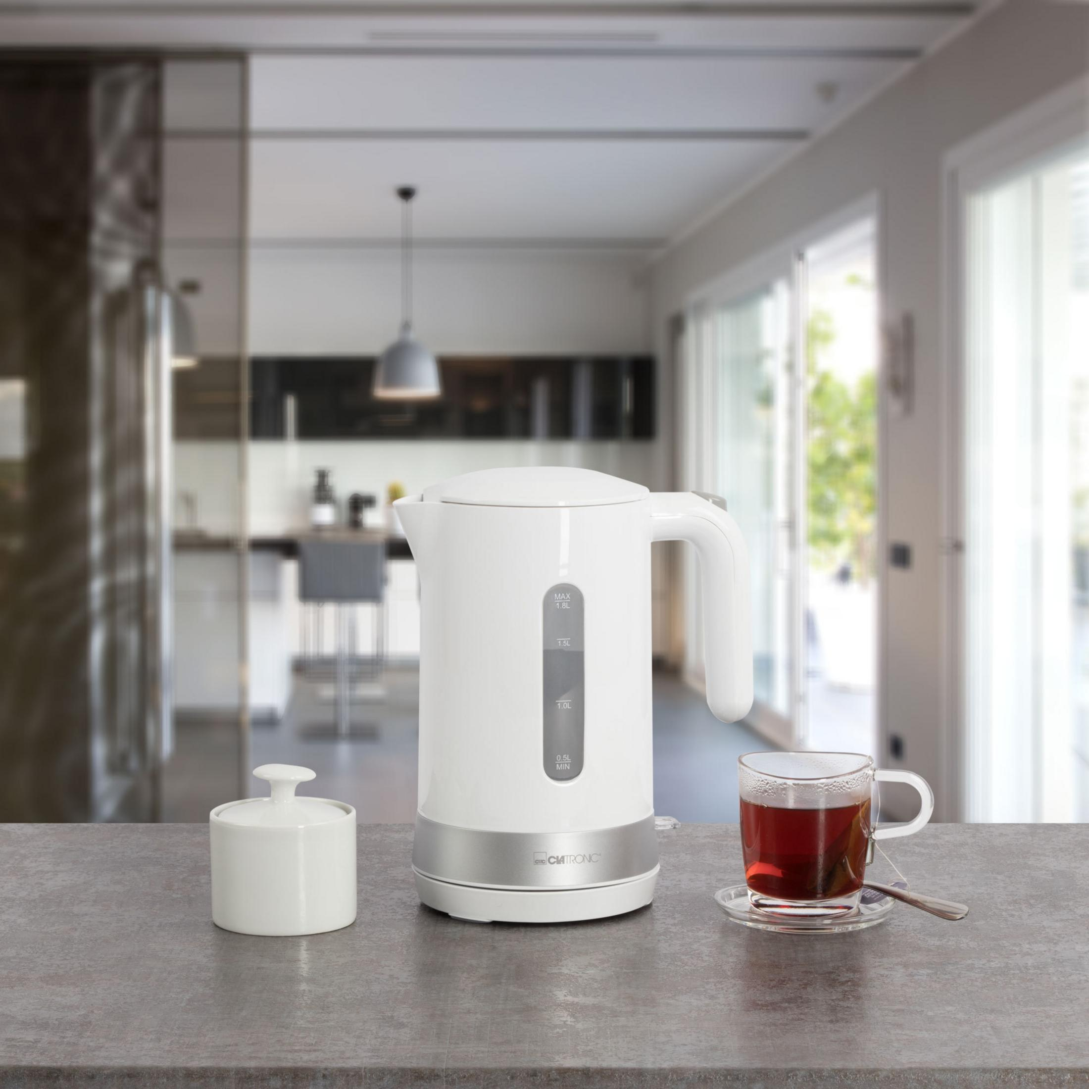 Weißer Wasserkocher auf einer Arbeitsplatte mit einer Teetasse, Zuckerdose und Küchenhintergrund.