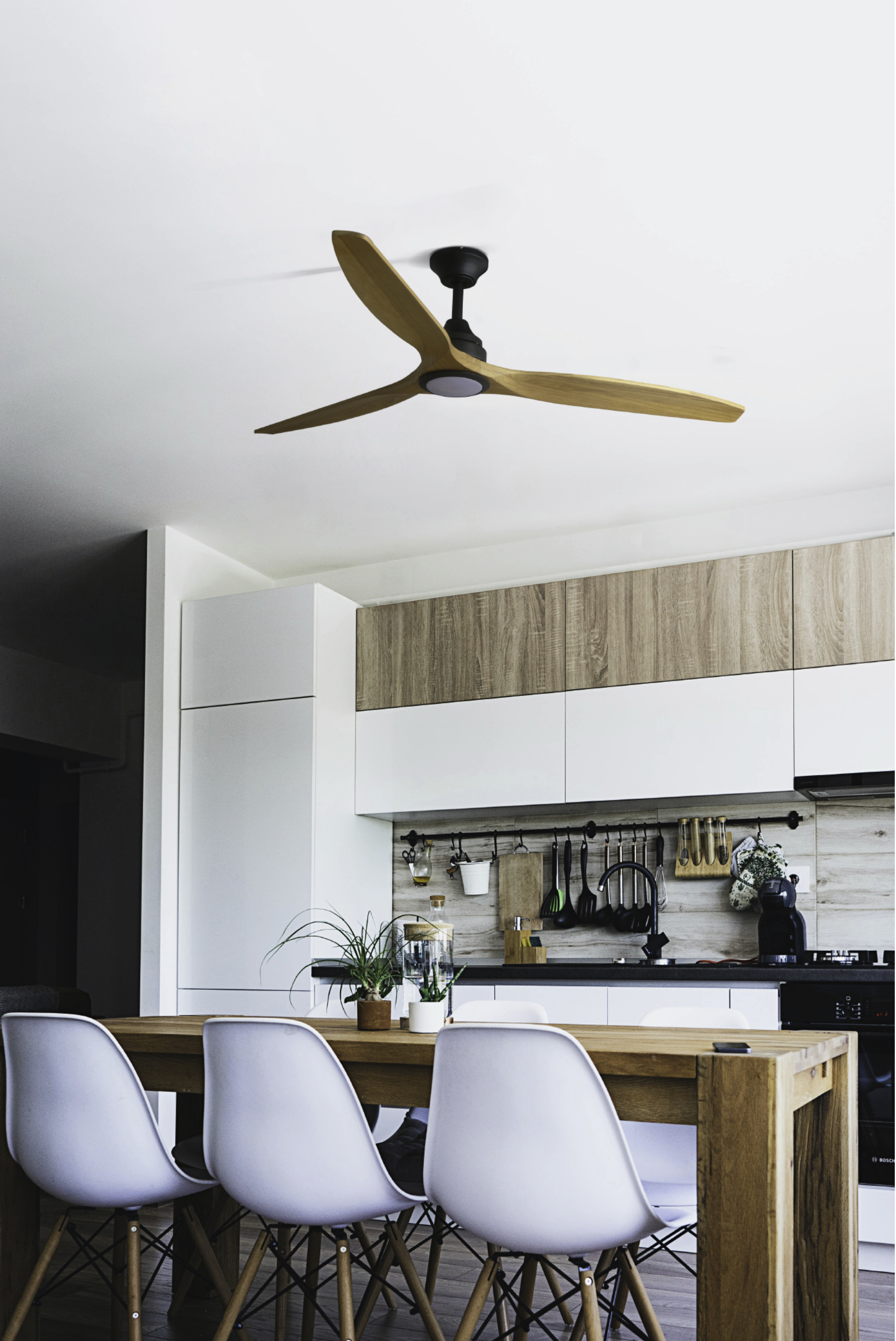 Una cucina moderna con un ventilatore a soffitto in legno, armadi bianchi e un tavolo di legno.
