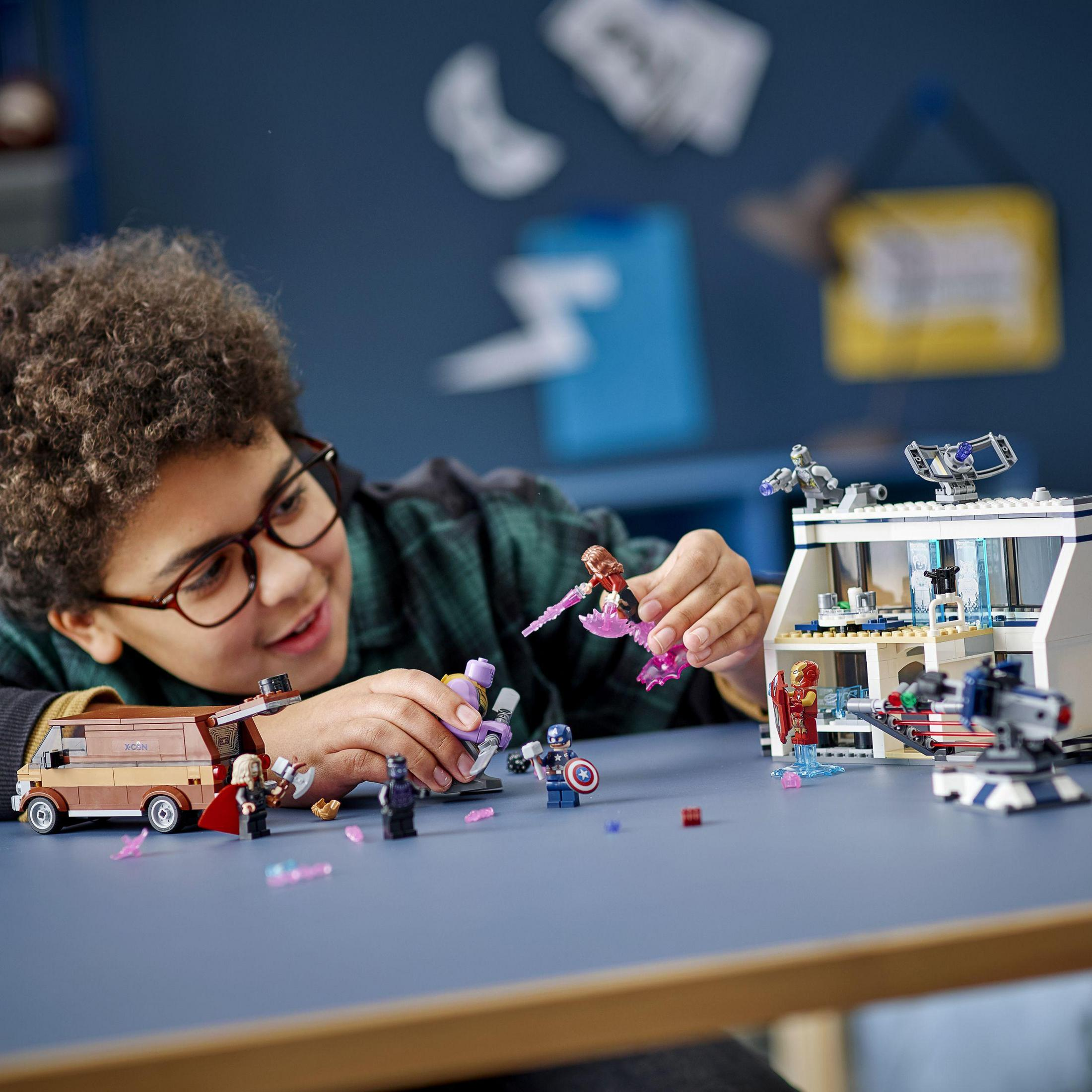 Un ragazzo gioca con i Lego. Sta costruendo un set Lego degli Avengers. Ci sono figure e strutture Lego.