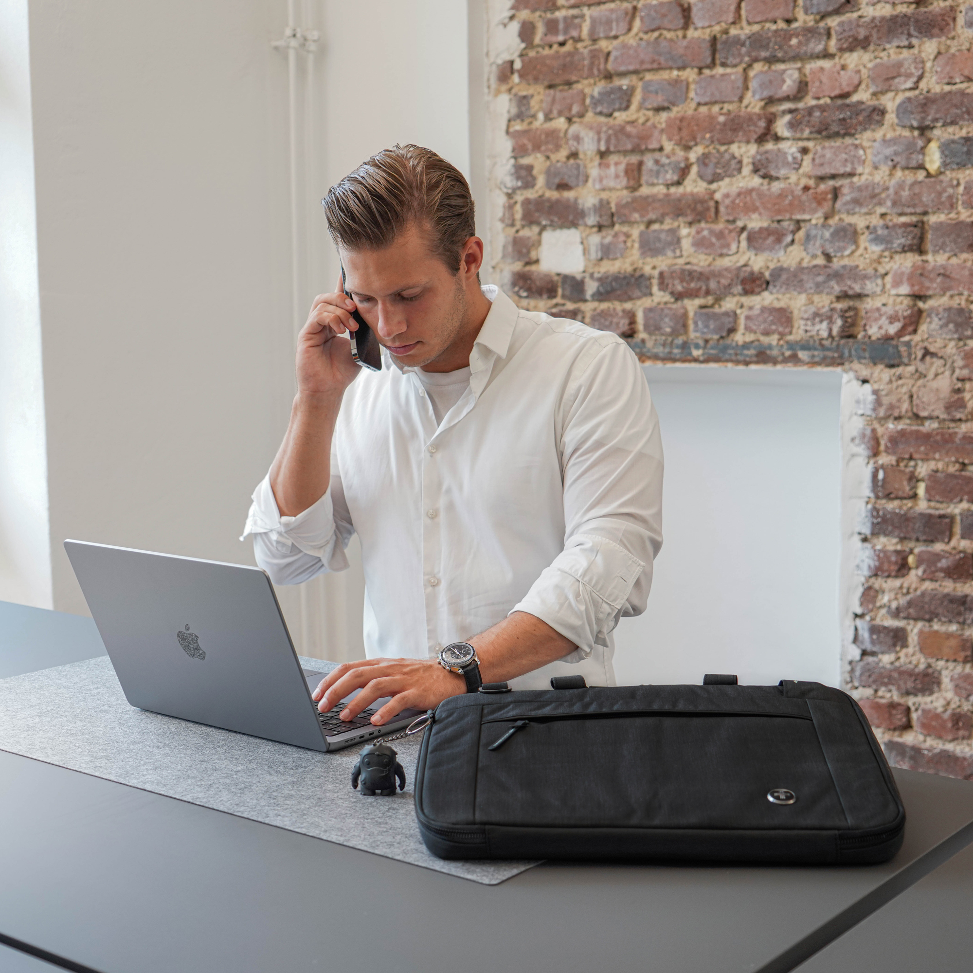 Uomo al telefono che lavora su un laptop. Borsa nera e statua vicina.