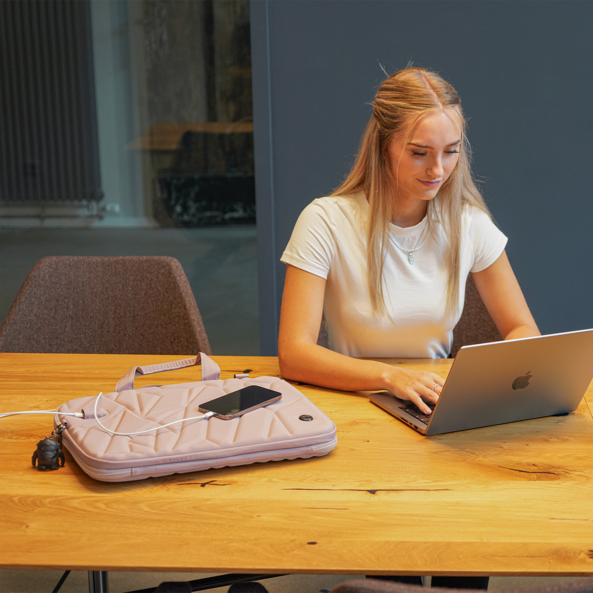 Donna che lavora su un laptop a un tavolo di legno, con telefono e borsa.