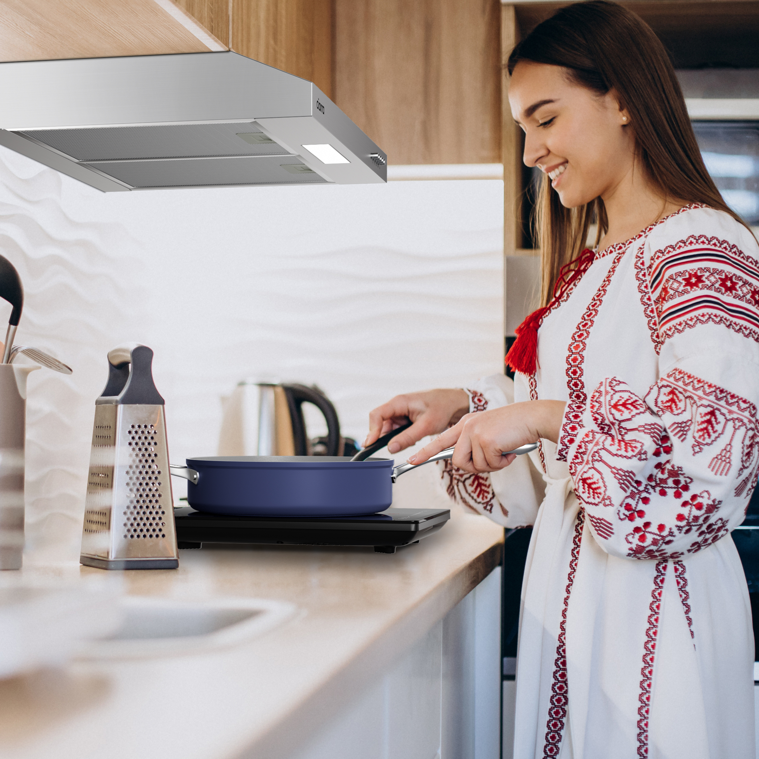 Een vrouw in een witte geborduurde jurk kookt in een keuken, met een blauwe pan op een fornuis.