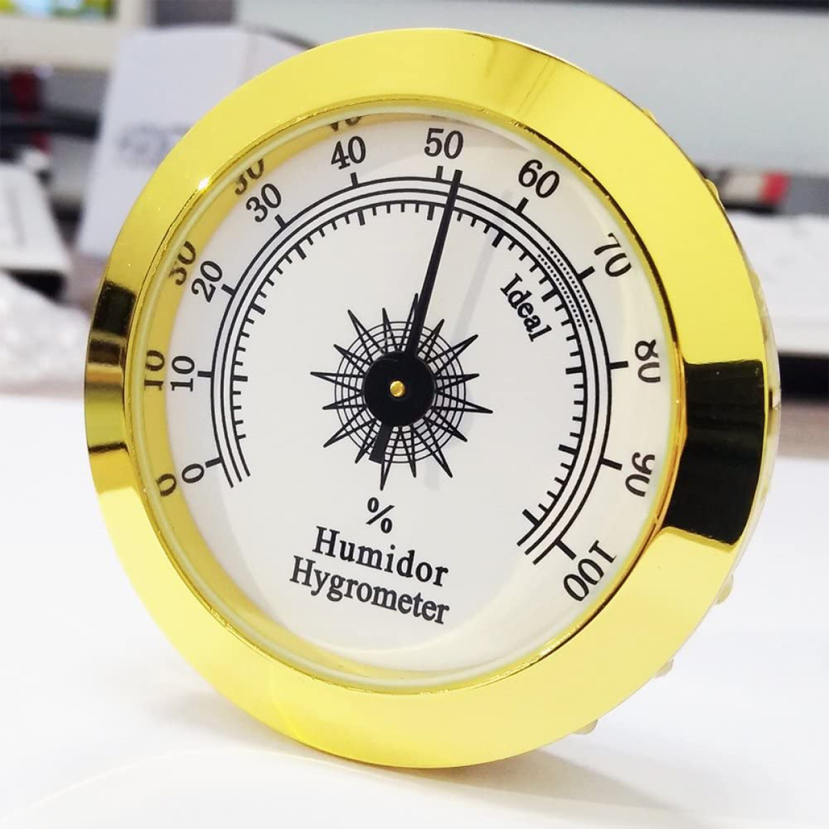 Ein goldgerahmtes Hygrometer zeigt die Luftfeuchtigkeit in Prozent an. Der ideale Bereich ist markiert. Weißer Hintergrund.