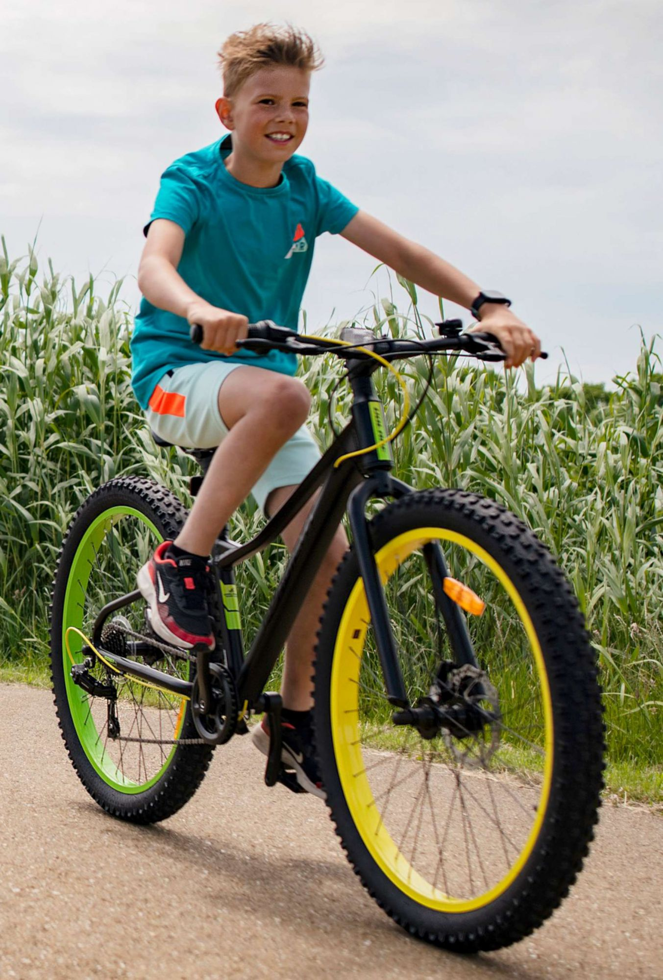 Junge auf einem Fahrrad. Schwarzes und gelbes Fahrrad. Der Junge lächelt. Grüne und gelbe Räder auf einem Feldweg.