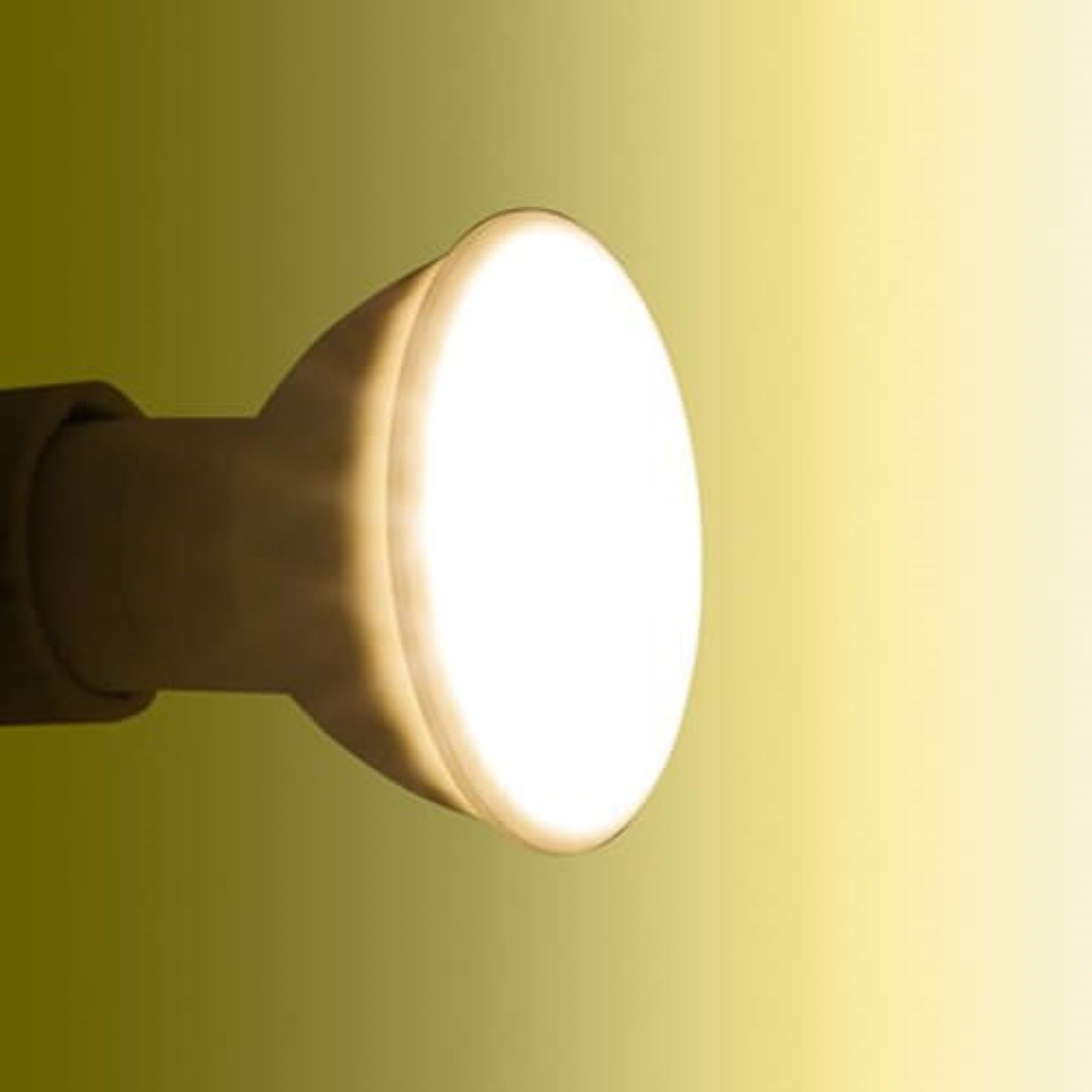 Eine helle, fokussierte Glühbirne, die gelbes Licht vor einem gelb-grünen Hintergrund aussendet.
