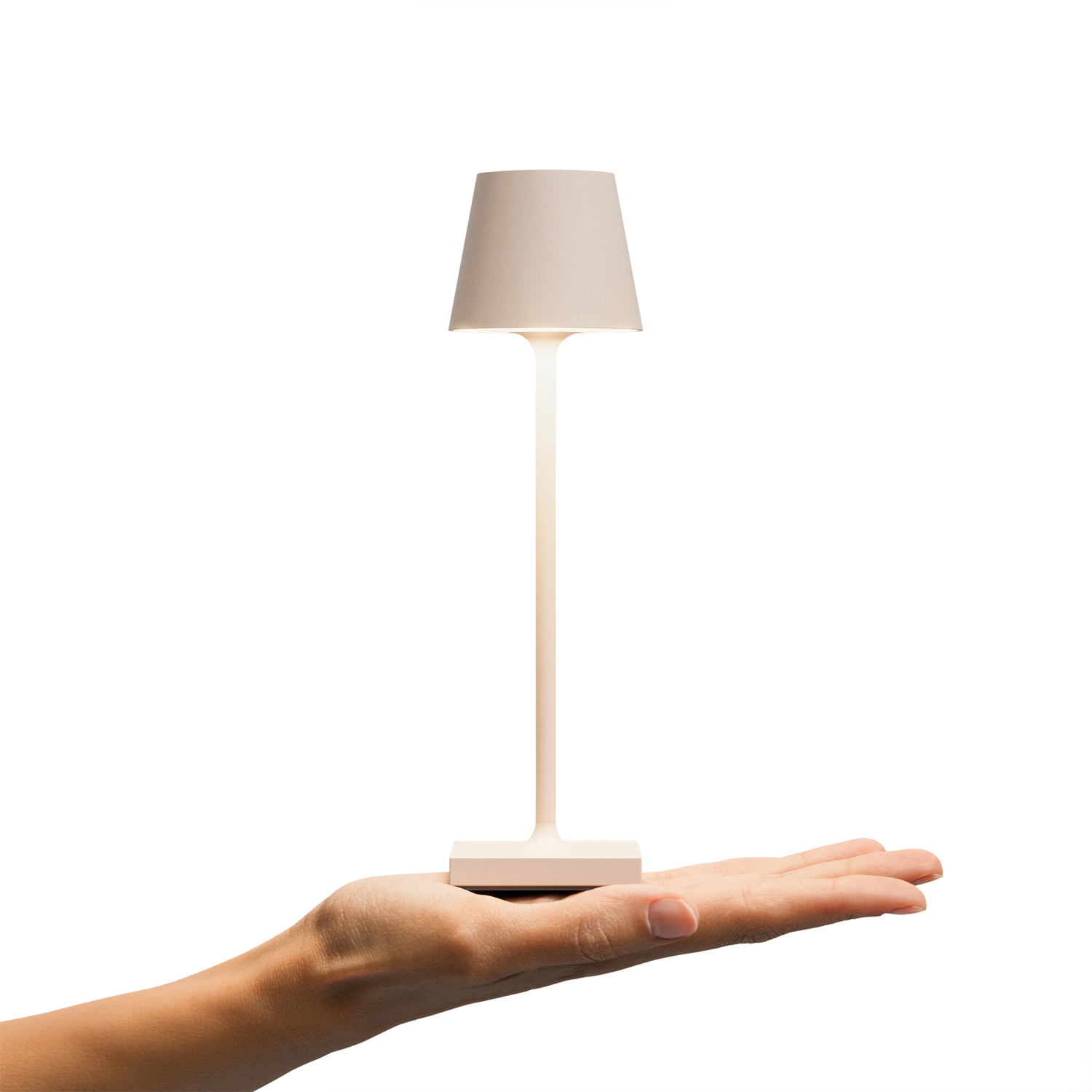 Eine Hand hält eine beige Tischlampe mit hohem Stiel und quadratischem Sockel.