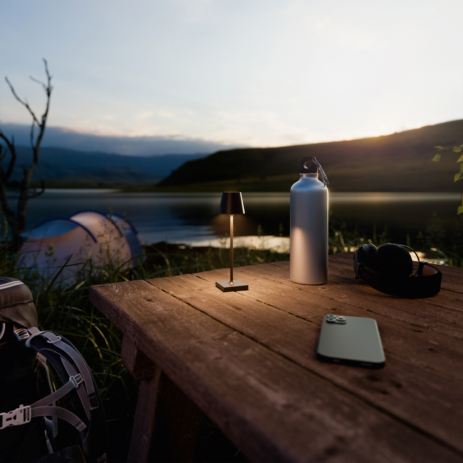 Ein Tisch mit Lampe, Wasserflasche, Telefon und Kopfhörern. Der Hintergrund ist ein See bei Sonnenuntergang.