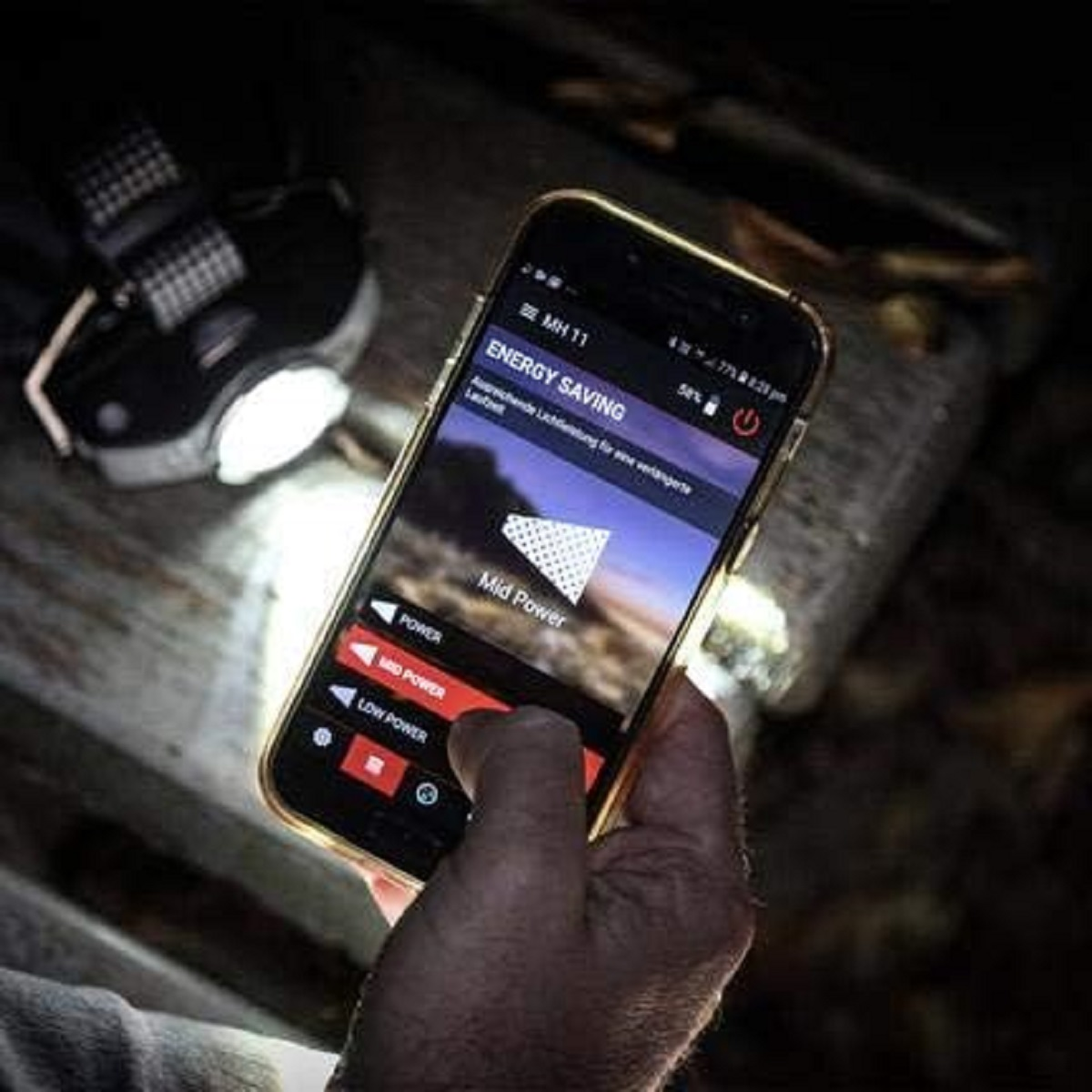 Eine Hand, die ein Telefon hält, das eine Energiespar-App-Oberfläche zeigt, mit einer Stirnlampe im Hintergrund.