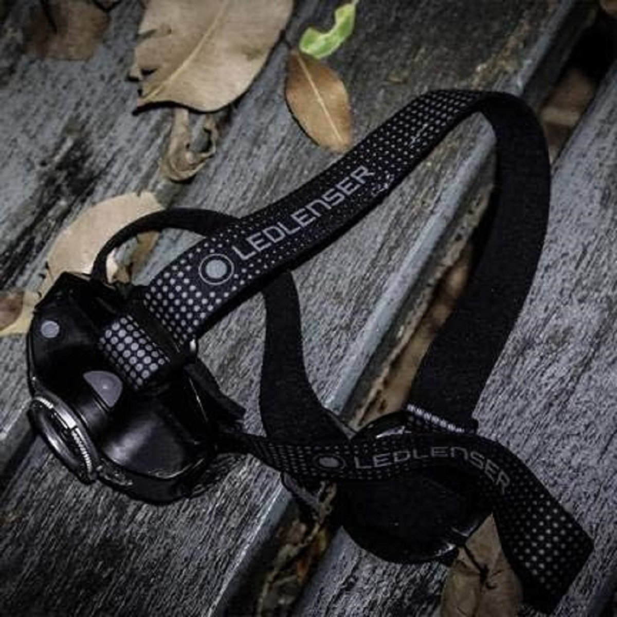 Eine schwarze LEDLENSER Stirnlampe auf einer Holzoberfläche. Sie hat schwarze Gurte mit dem LEDLENSER-Logo.