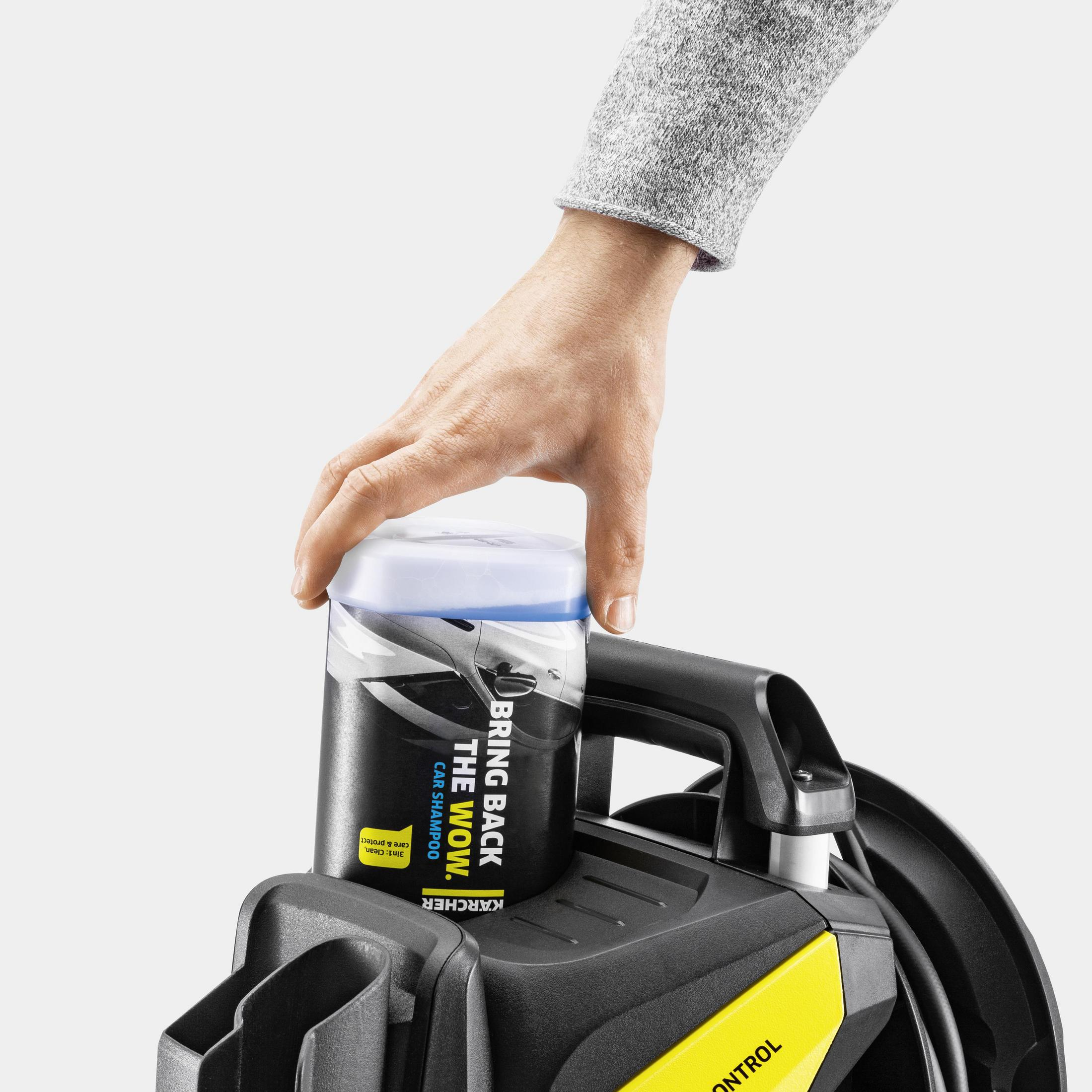 Hand hält eine Autoshampoo-Flasche über einem schwarz-gelben Kärcher-Hochdruckreiniger.