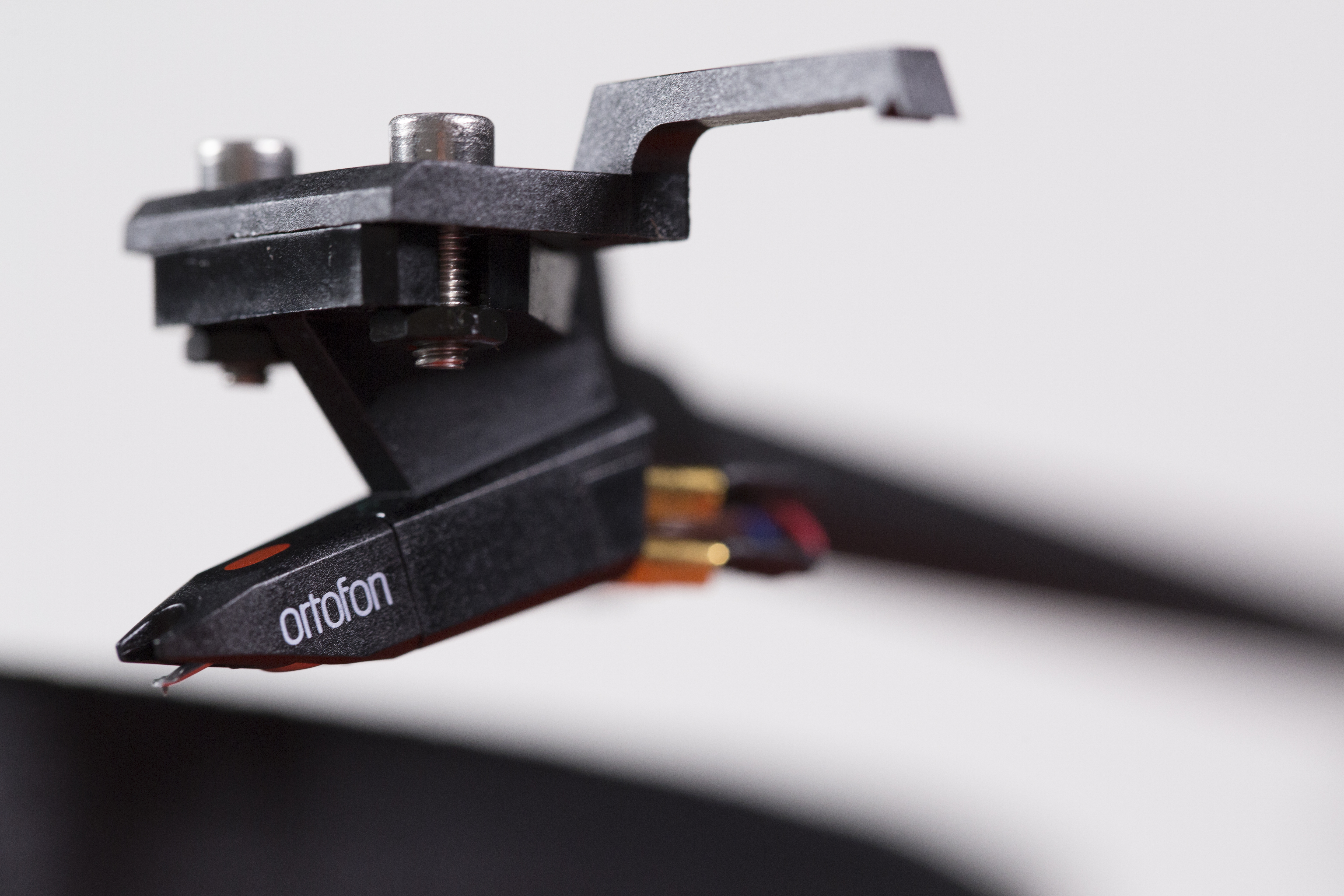 Close-up van een zwarte Ortofon-cartridge met een rode stylus op een witte achtergrond.