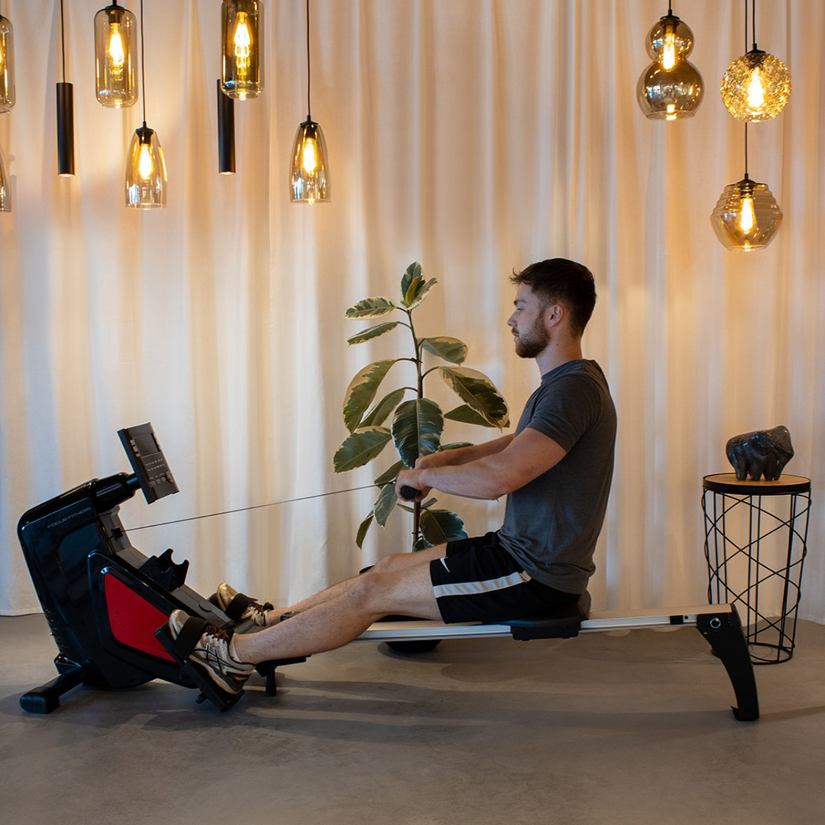 Man exercising on a rowing machine. Various lights hang from the ceiling.