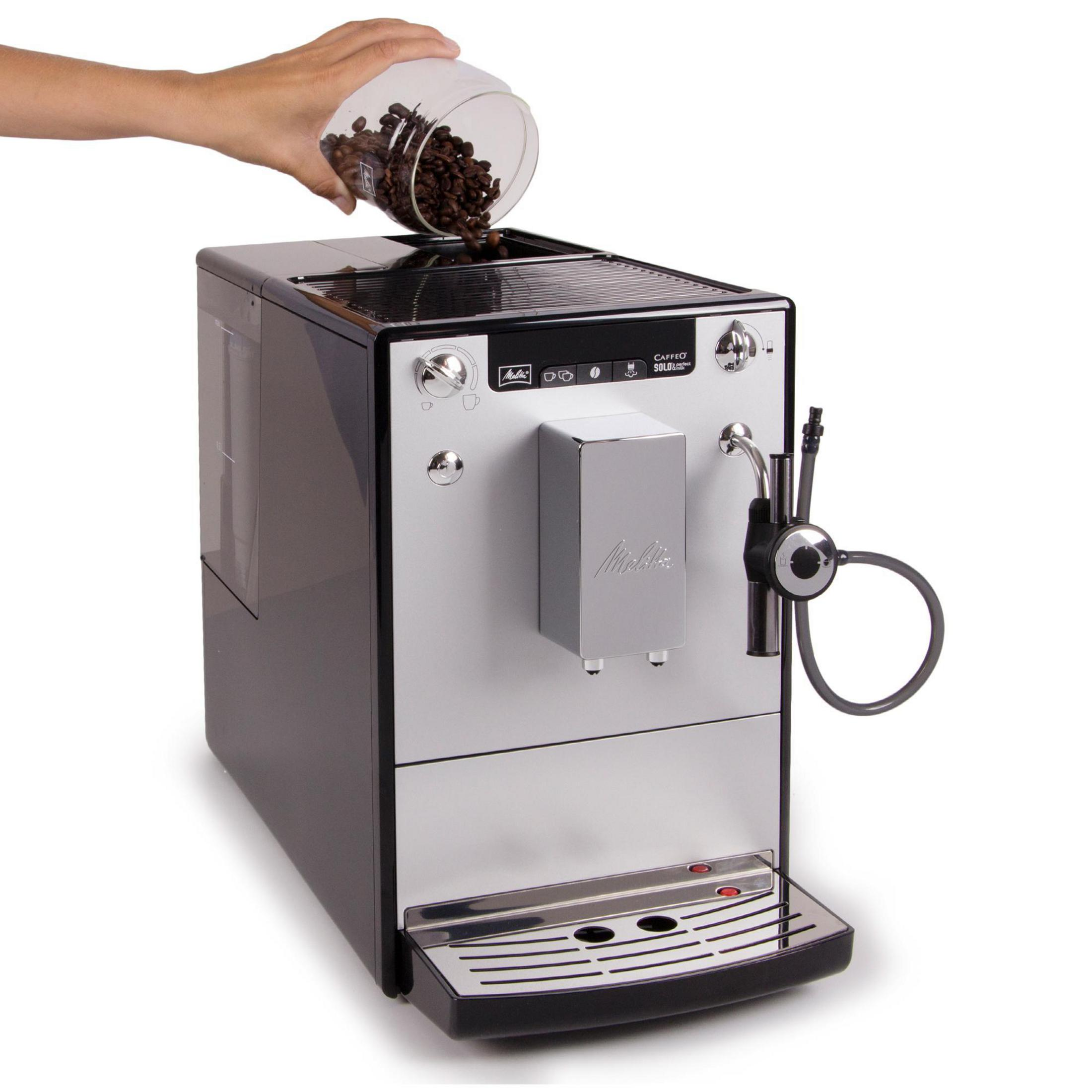 Kaffeemaschine, in die von einer Hand Kaffeebohnen gegossen werden. Weißer Hintergrund.