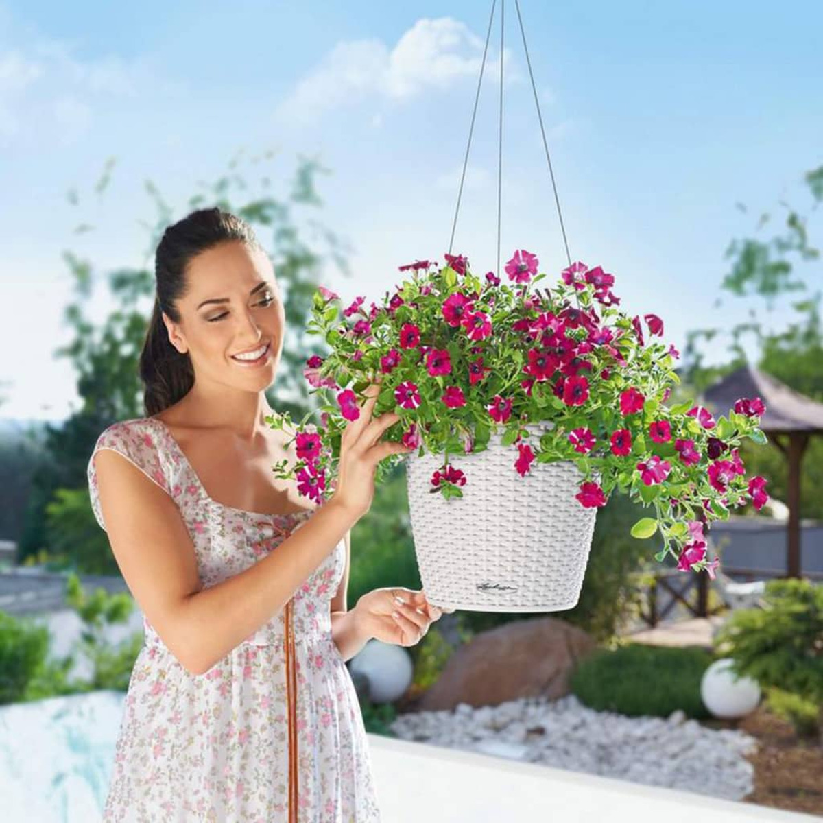 Frau hält einen weißen Hängekorb mit lila Blumen.