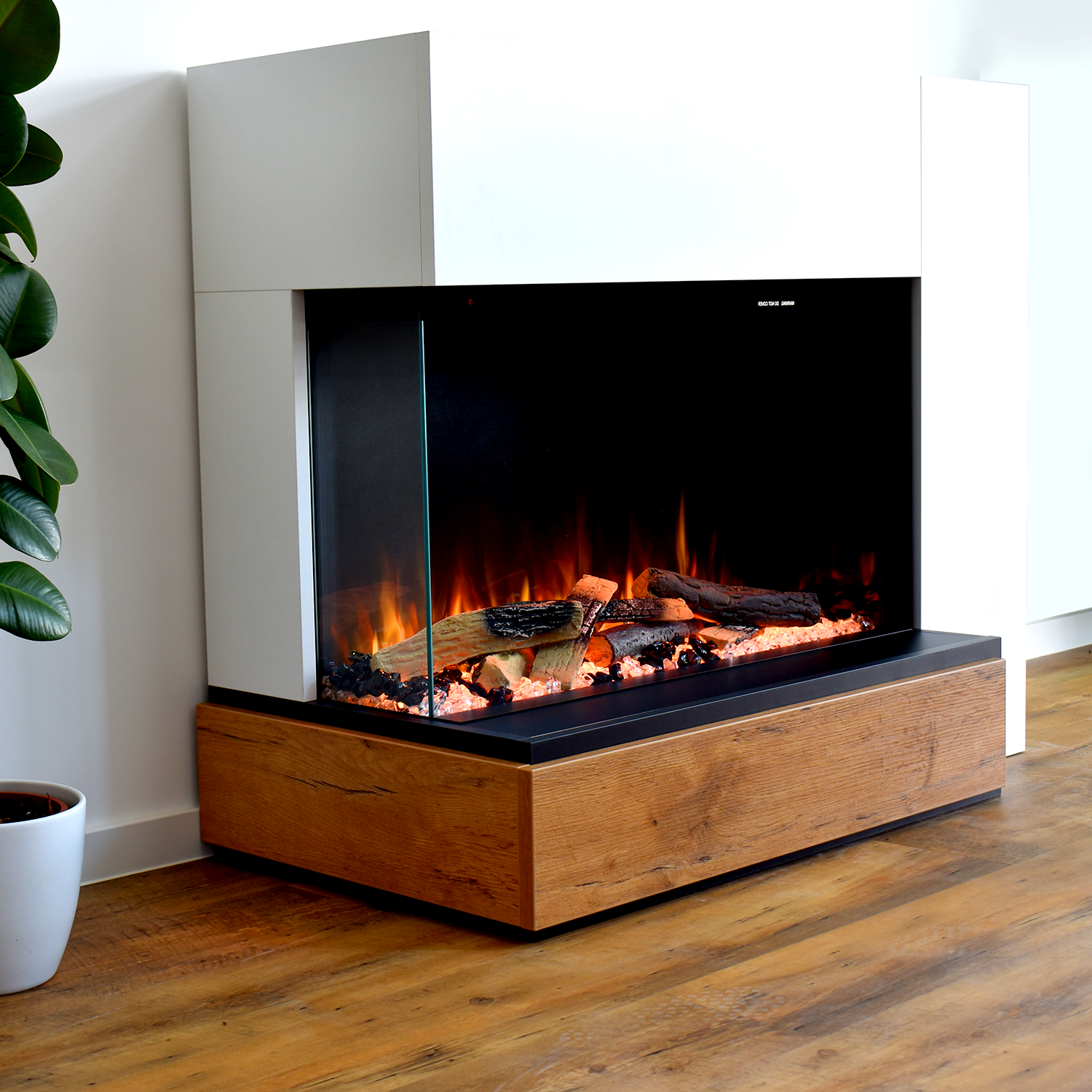 Elektrokamin mit Holzsockel und Glasfront, mit brennenden Holzscheiten. Weiße Wand im Hintergrund.