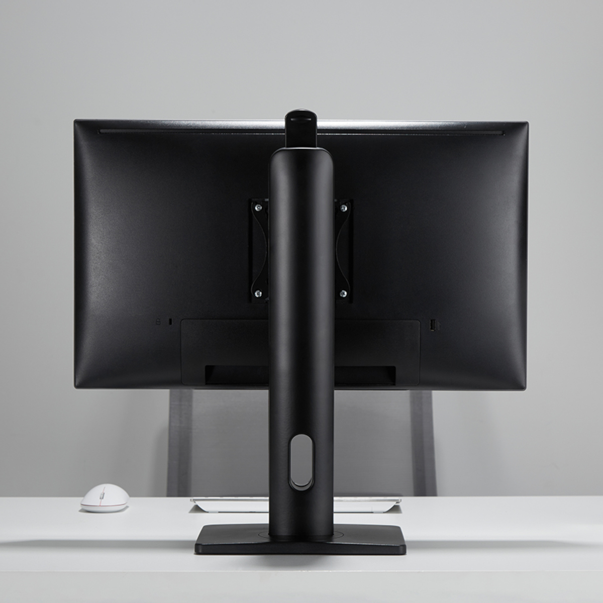 Rückansicht eines schwarzen Computermonitors mit schwarzem Ständer auf einem weißen Schreibtisch. Eine Maus daneben.
