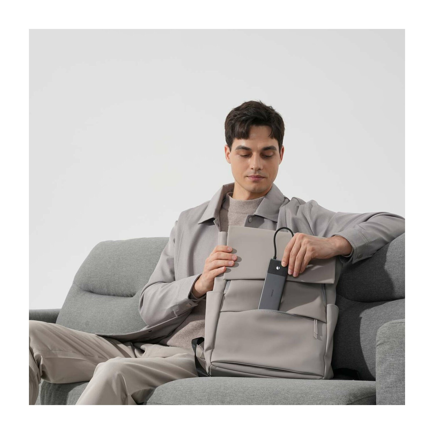 Mann sitzt auf einem Sofa und packt einen grauen Rucksack aus.