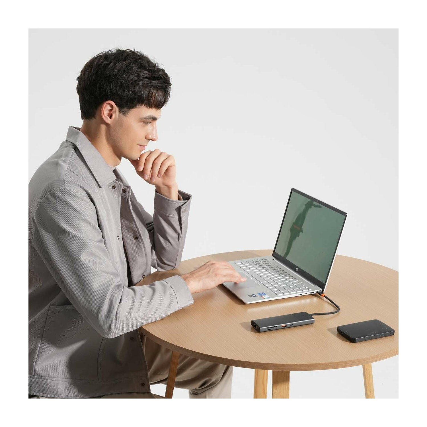 Mann sitzt an einem runden Tisch und benutzt einen Laptop. Ein Hub und eine externe Festplatte liegen daneben.