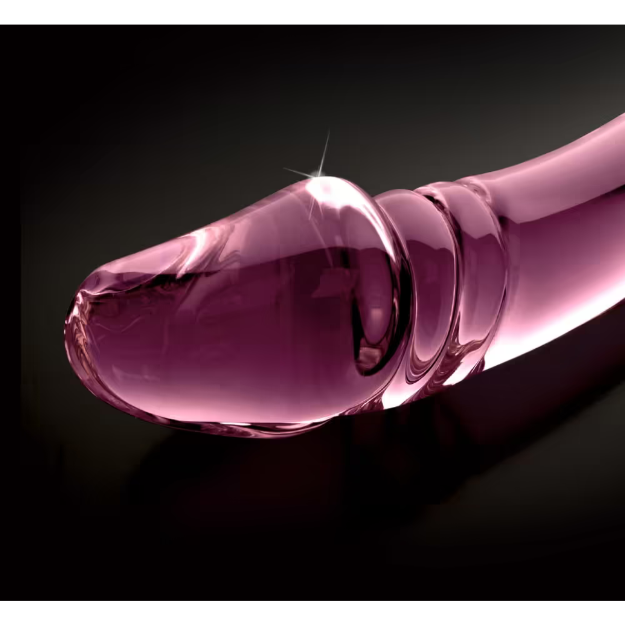 Nahaufnahme eines rosa Glasdildos auf schwarzer Oberfläche.