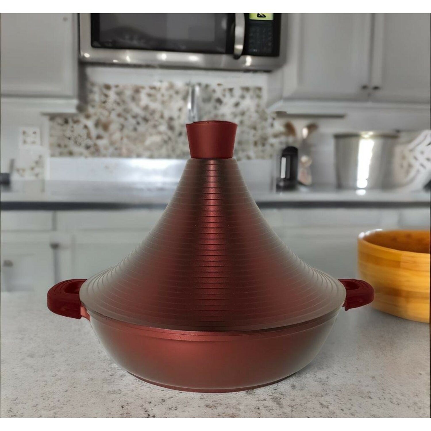 Ein kastanienbrauner Tajine-Topf mit Griffen auf einer Arbeitsplatte in einer Küche.