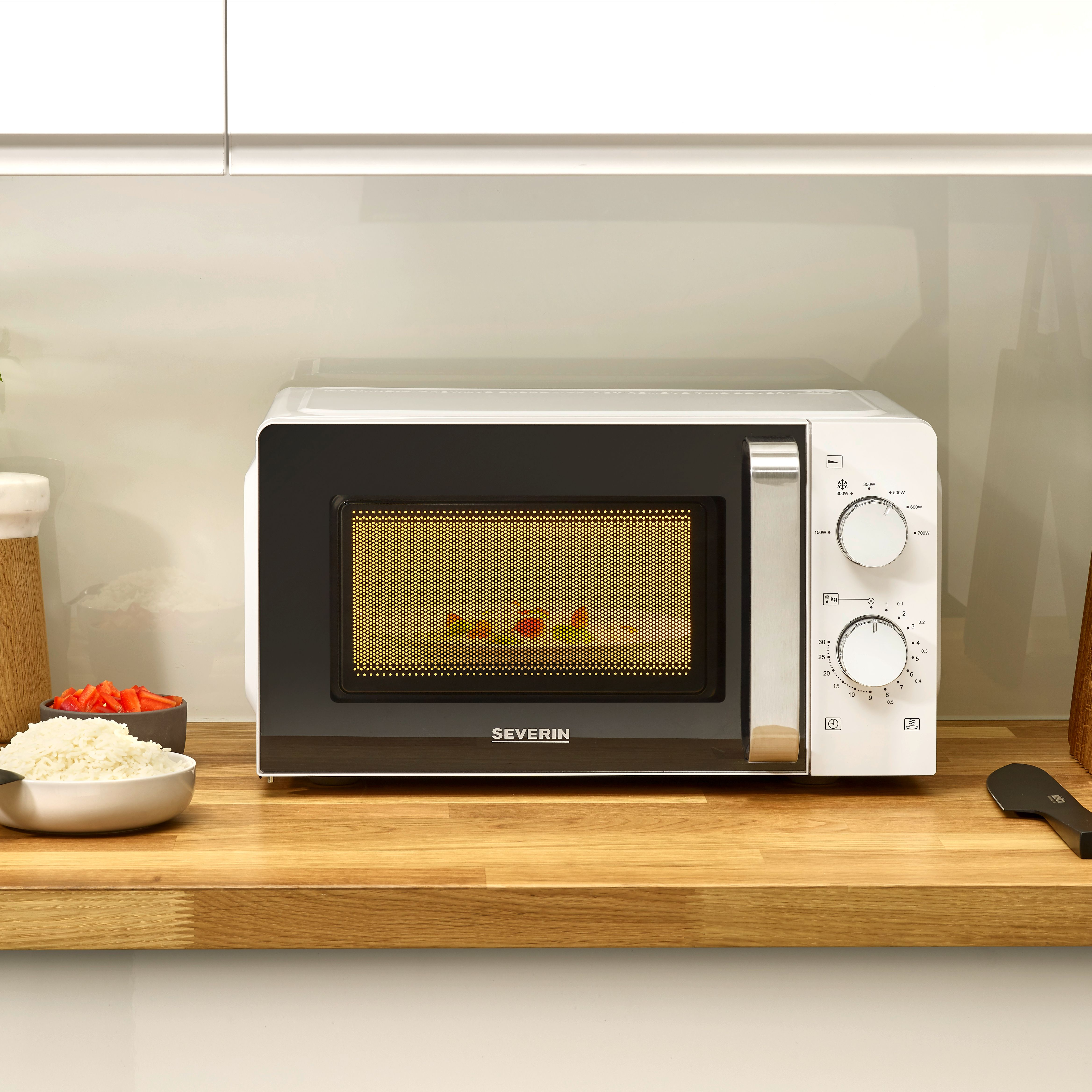 Biała kuchenka mikrofalowa z czarnymi drzwiami, sterowaniem po prawej i jedzeniem w środku. Drewniany blat.