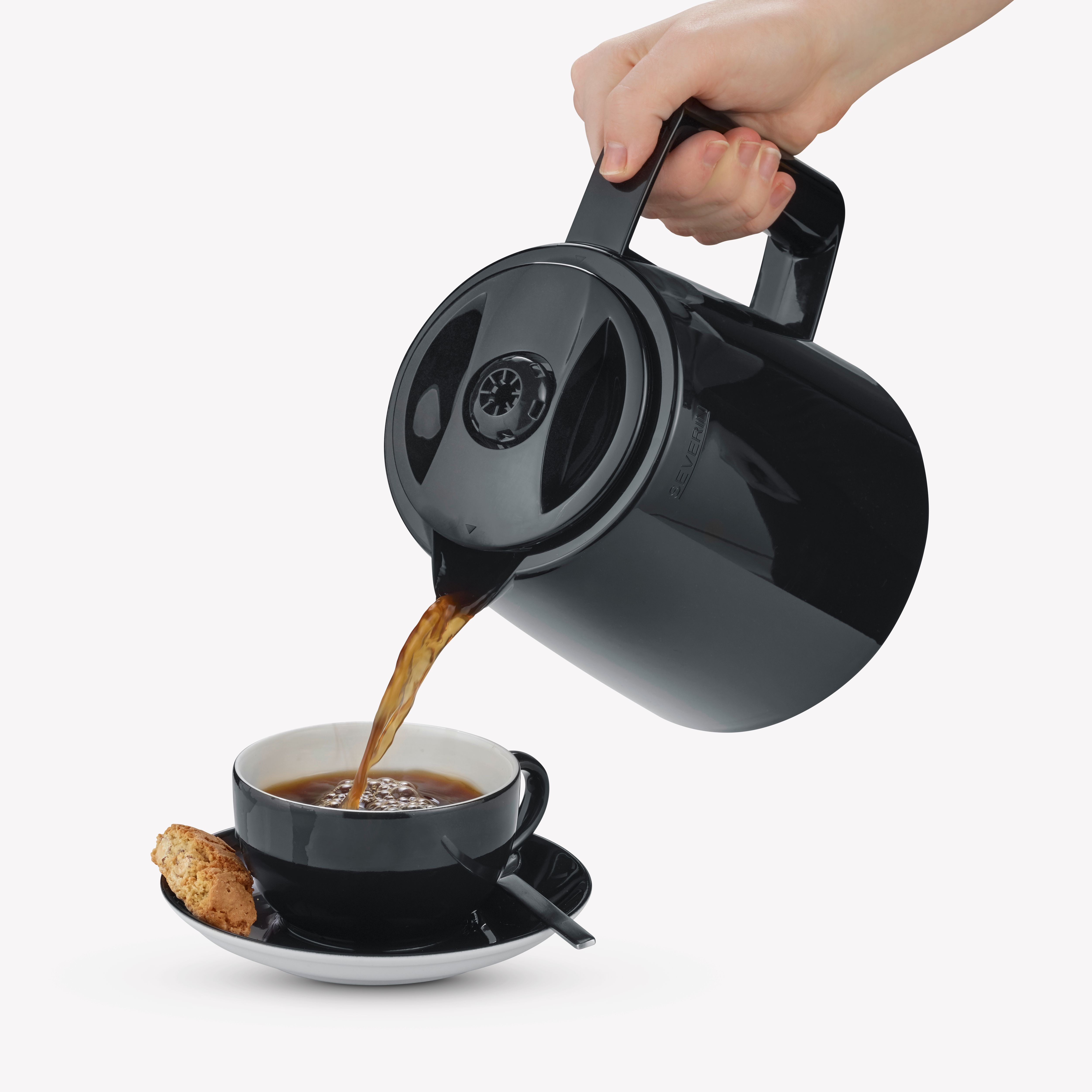 Ręka nalewa kawę z czarnej karafki do czarnego kubka.