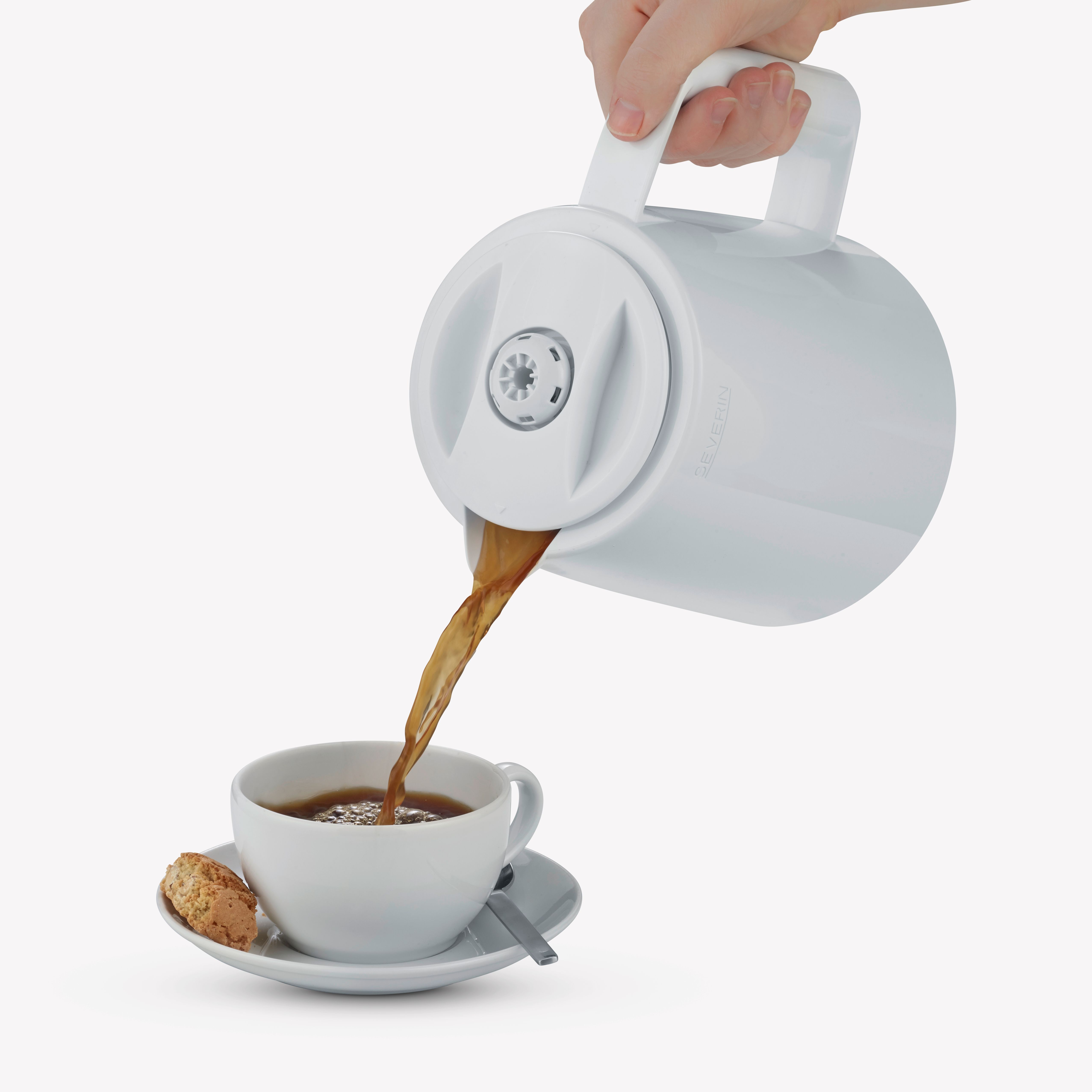 Osoba nalewa kawę z białego dzbanka do białej filiżanki na spodku z ciasteczkiem.