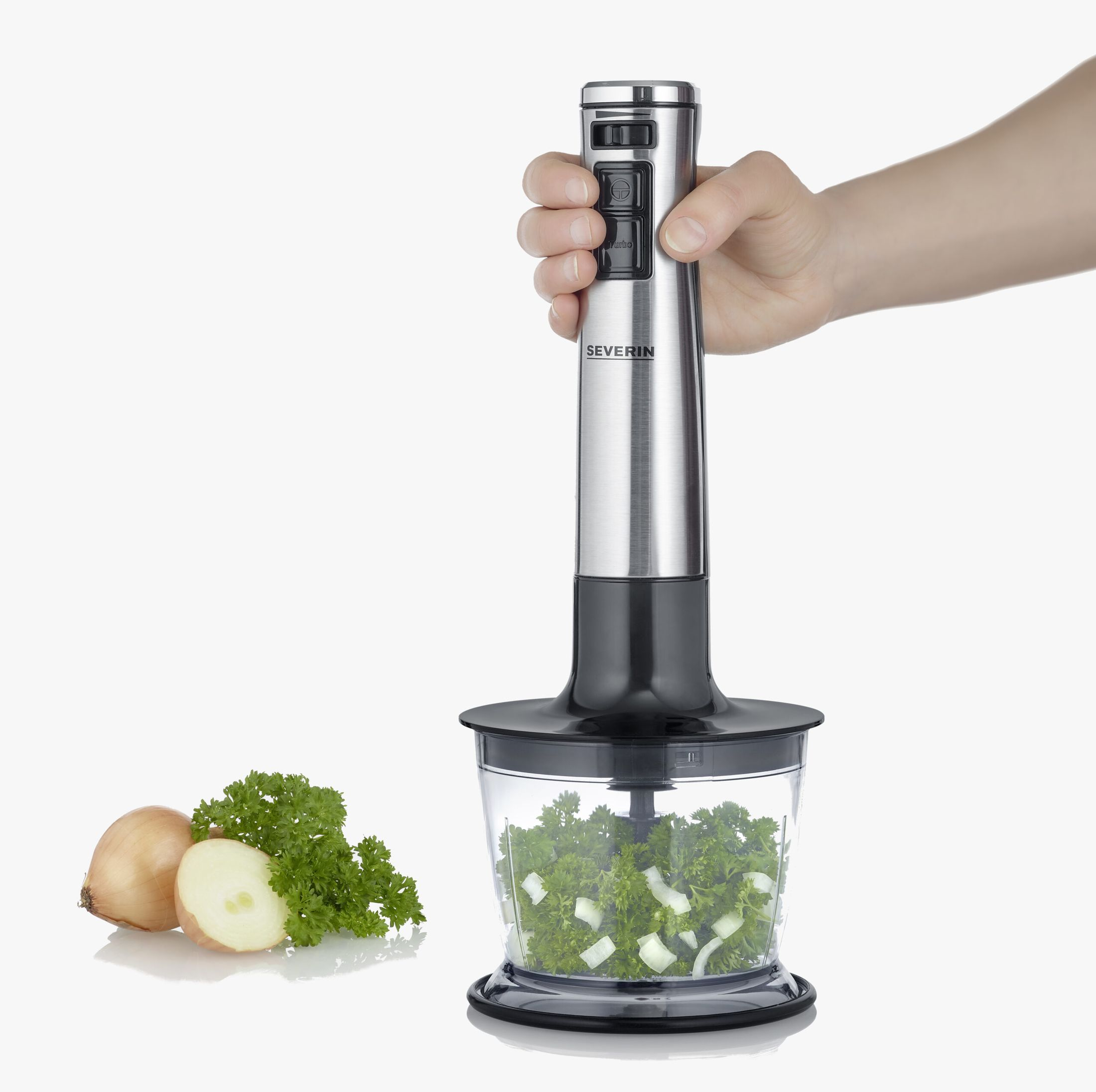Hand holding a silver immersion blender over chopped parsley and onion.