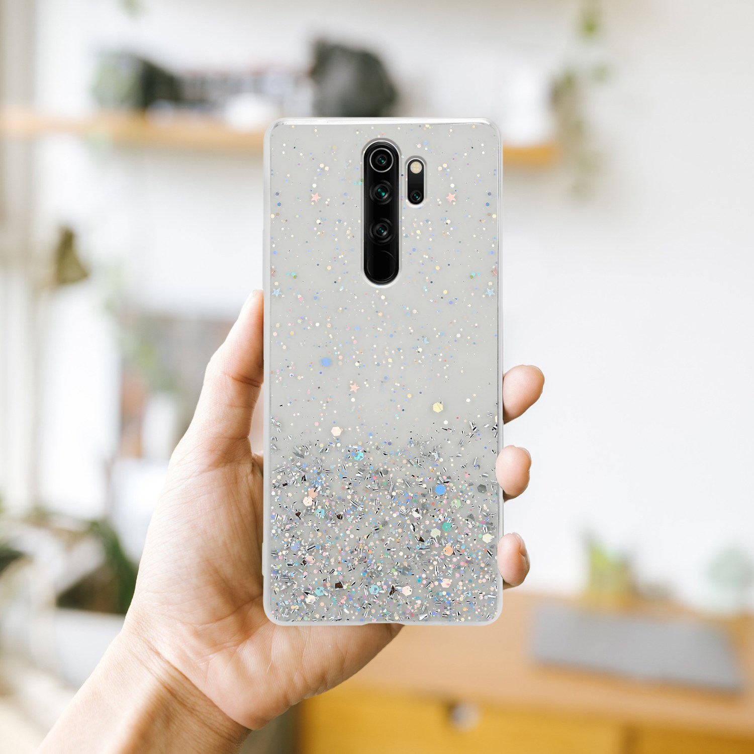 Mano che tiene una cover con glitter, sfondo sfocato.