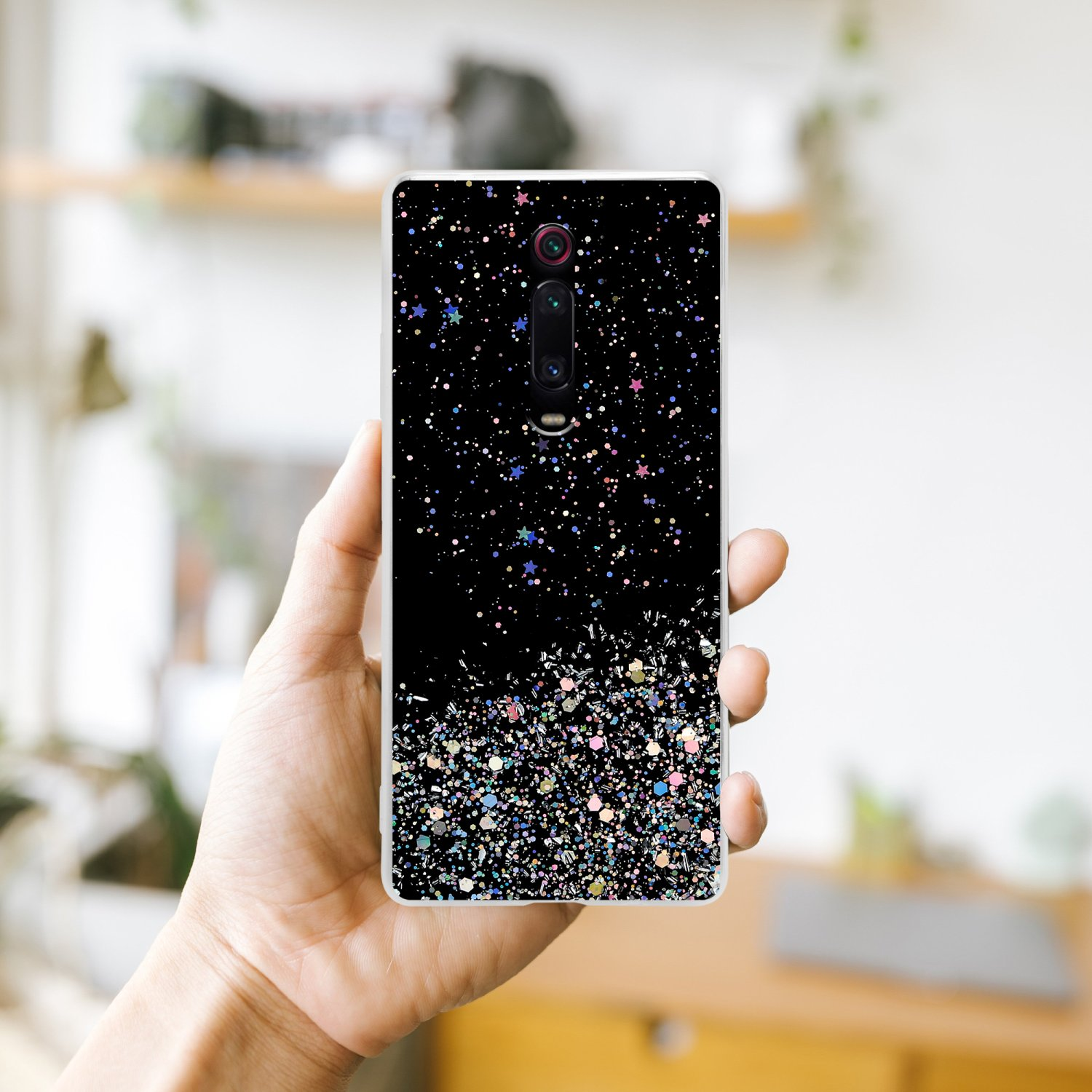 Mano che tiene una custodia per telefono con sfondo nero e glitter. Il telefono è visibile.