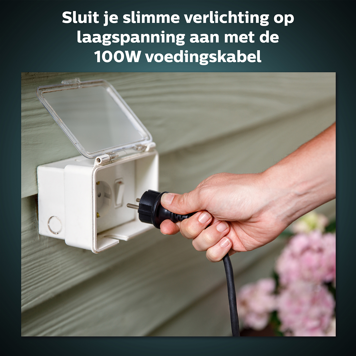 Eine Hand steckt ein schwarzes Netzkabel in eine weiße Außensteckdose mit niederländischem Text darüber.