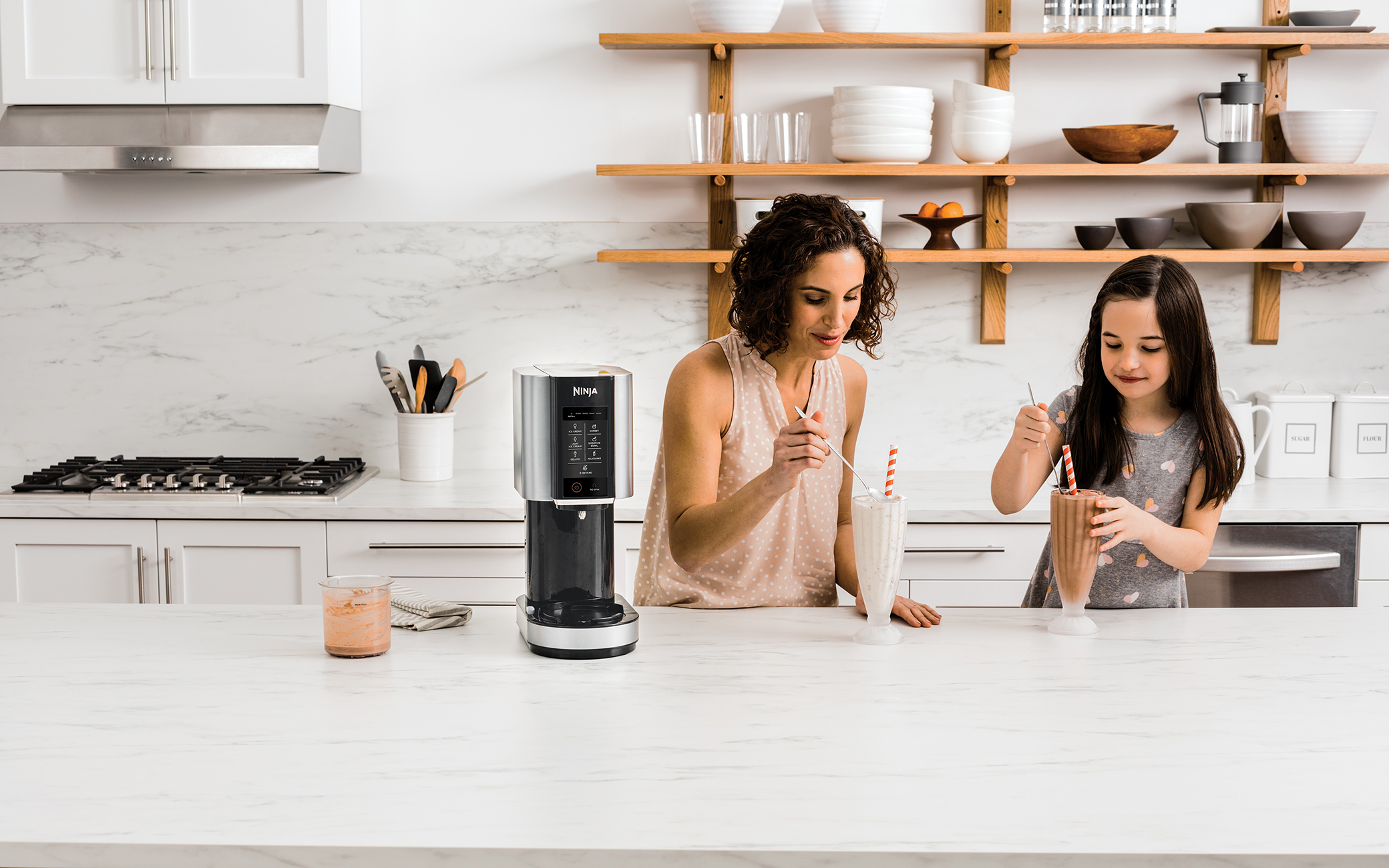 Kobieta i dziecko robią koktajle w kuchni z blenderem Ninja na blacie.