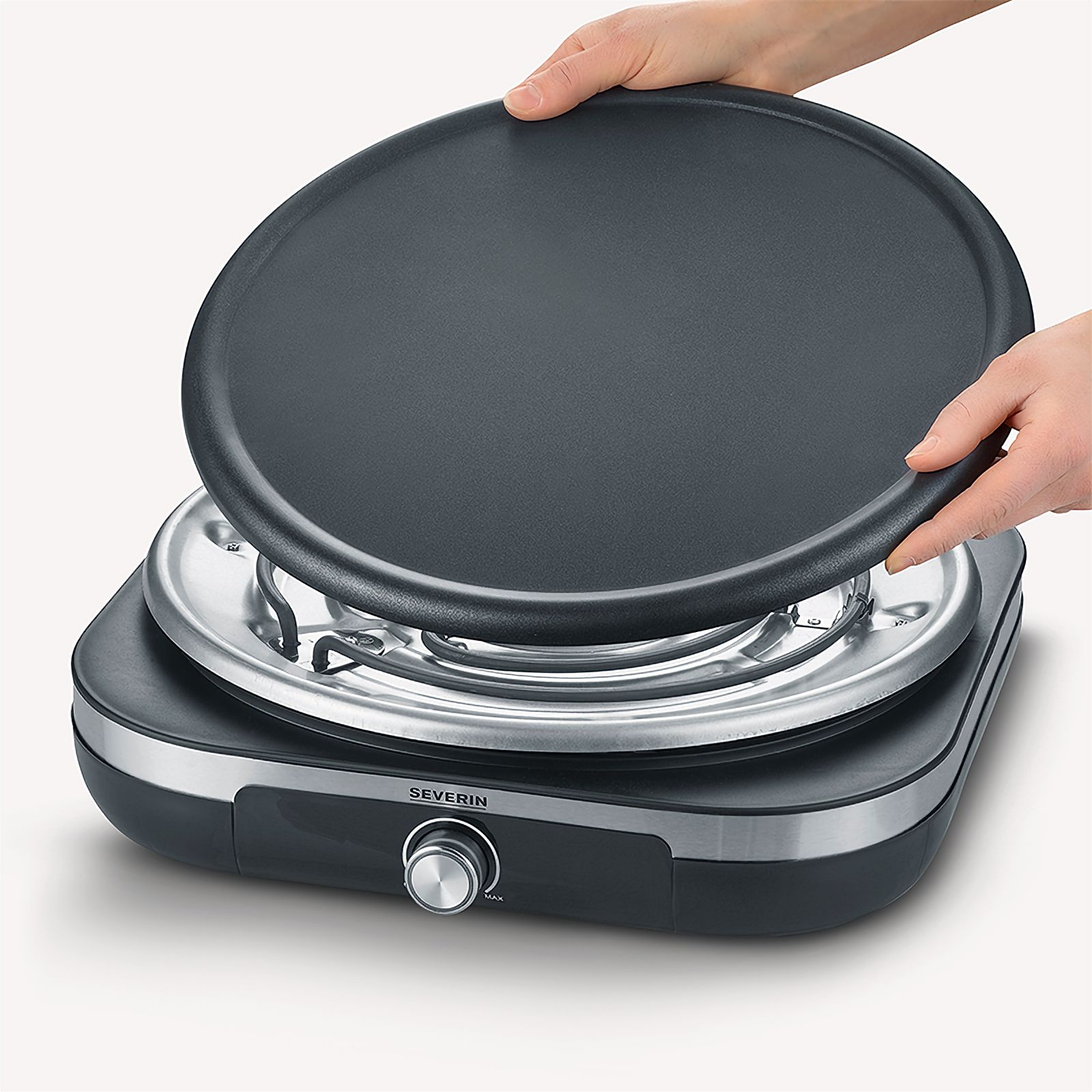 Ręce trzymają czarną, okrągłą patelnię nad czarnym i srebrnym urządzeniem.