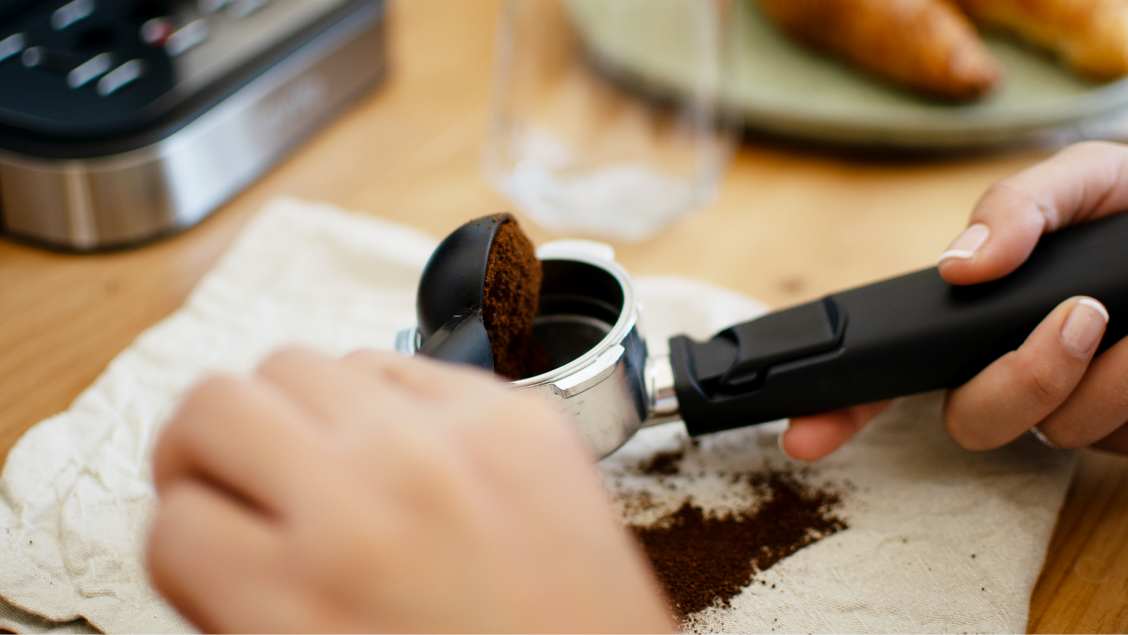 Manos llenando un portafiltro con café molido sobre un paño blanco, con un vaso.