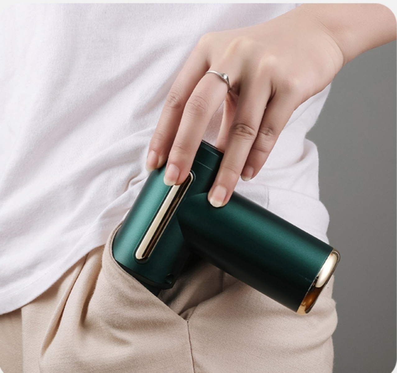 Una mano sostiene un dispositivo verde y dorado en un bolsillo. Fondo neutral.