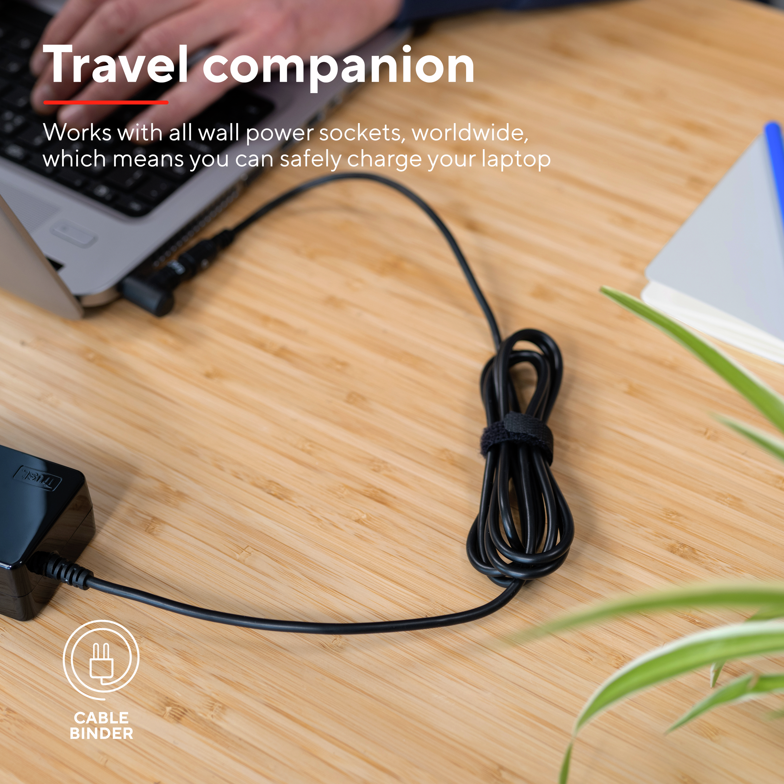 Personne utilisant un ordinateur portable avec un câble enroulé en boucle. Le câble est connecté à un adaptateur sur une surface en bois.