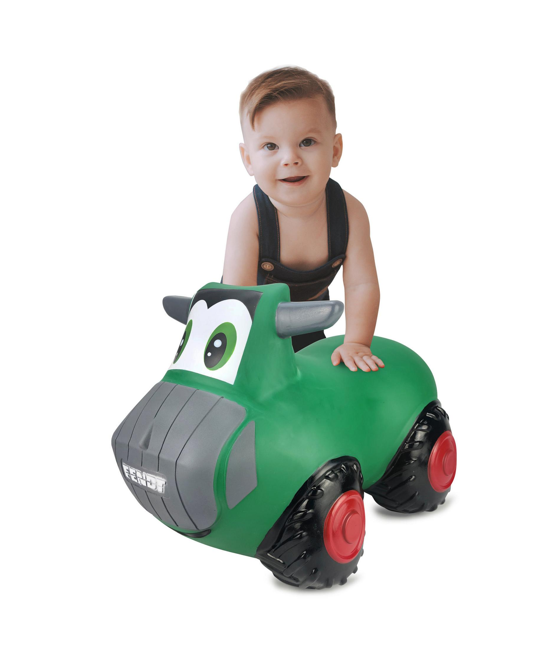 Małe dziecko na zielonym traktorze zabawce, uśmiechnięte, na białym tle.