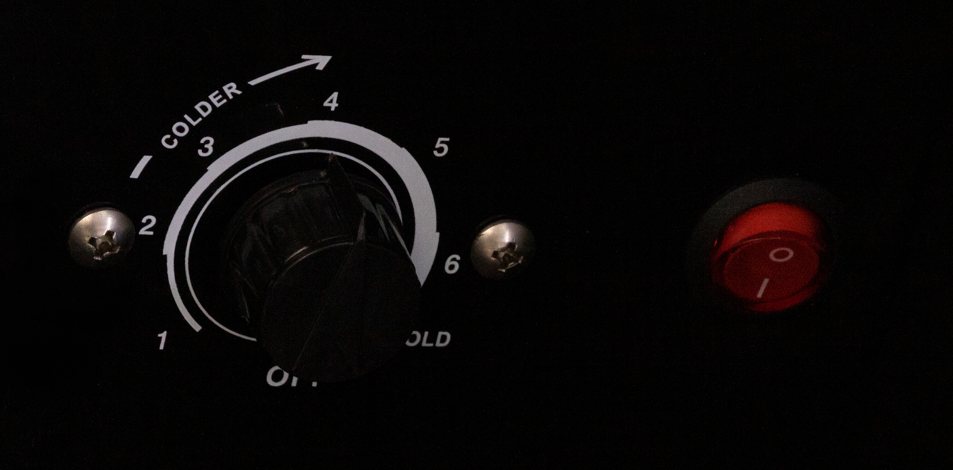 Close-up of a black appliance control knob. It is labeled with numbers and the word COLDER.