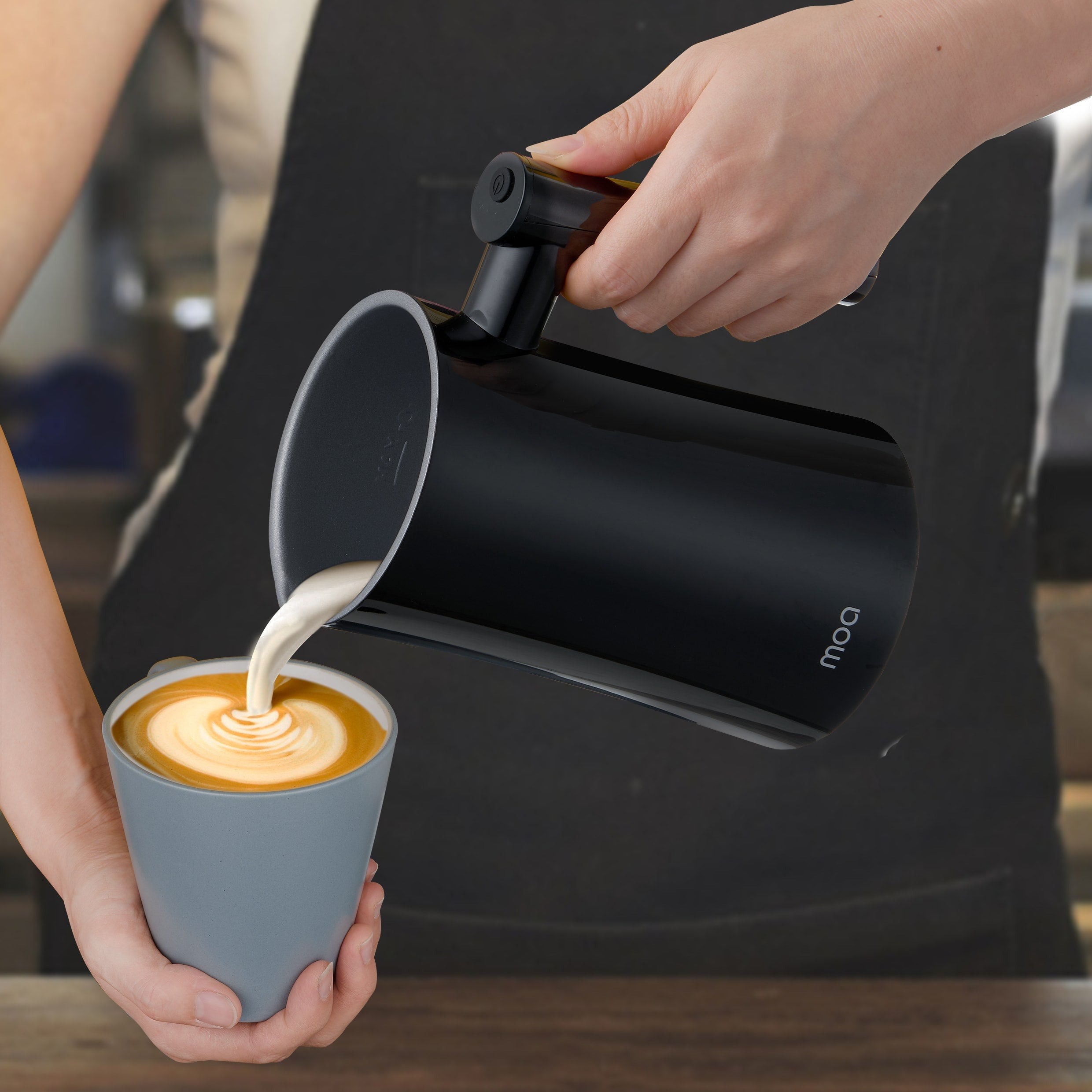 Handen schenken melk uit een zwarte kan in een grijze kop met koffie.