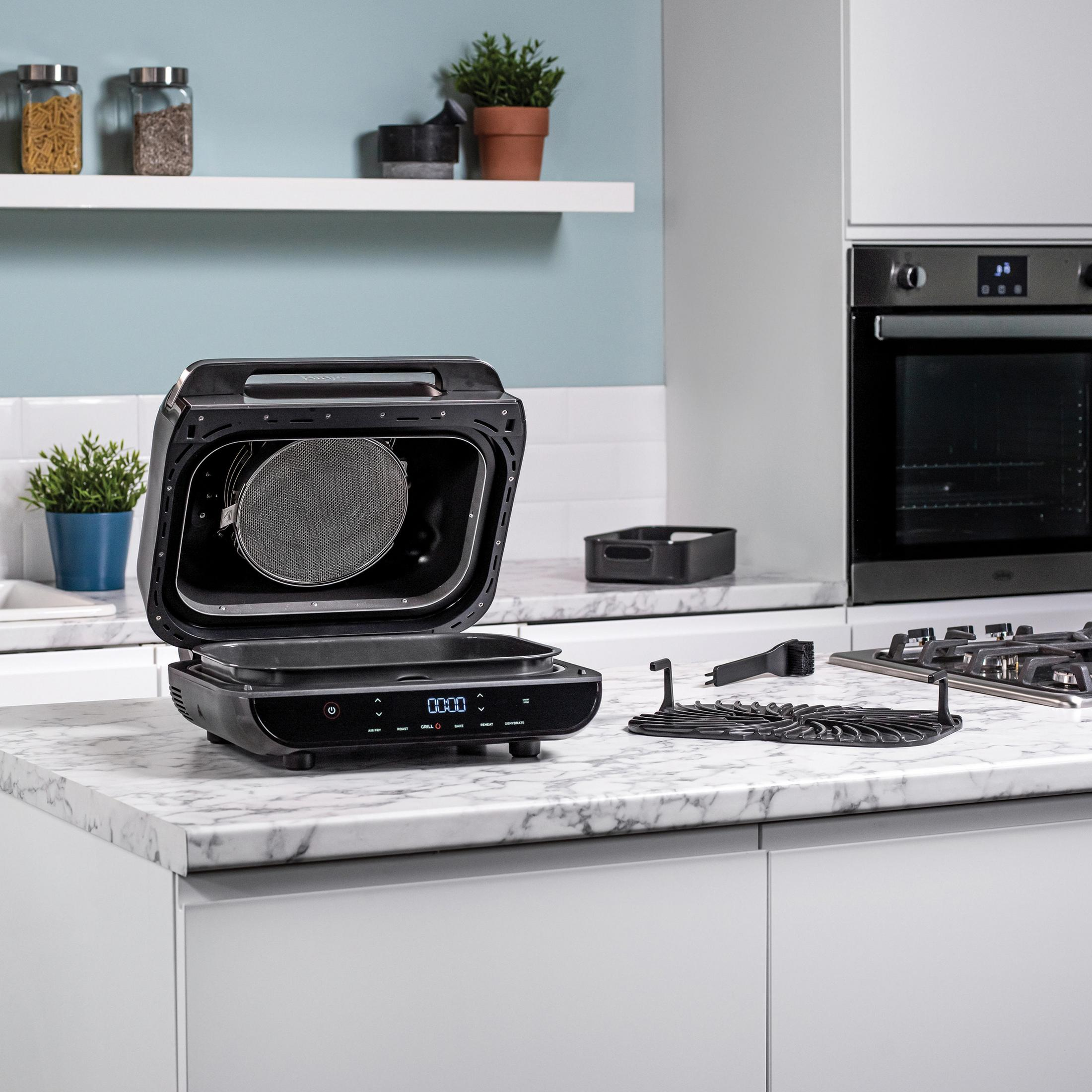 Otwarta czarna frytkownica na blacie z marmuru, z akcesoriami i gładkim tłem.