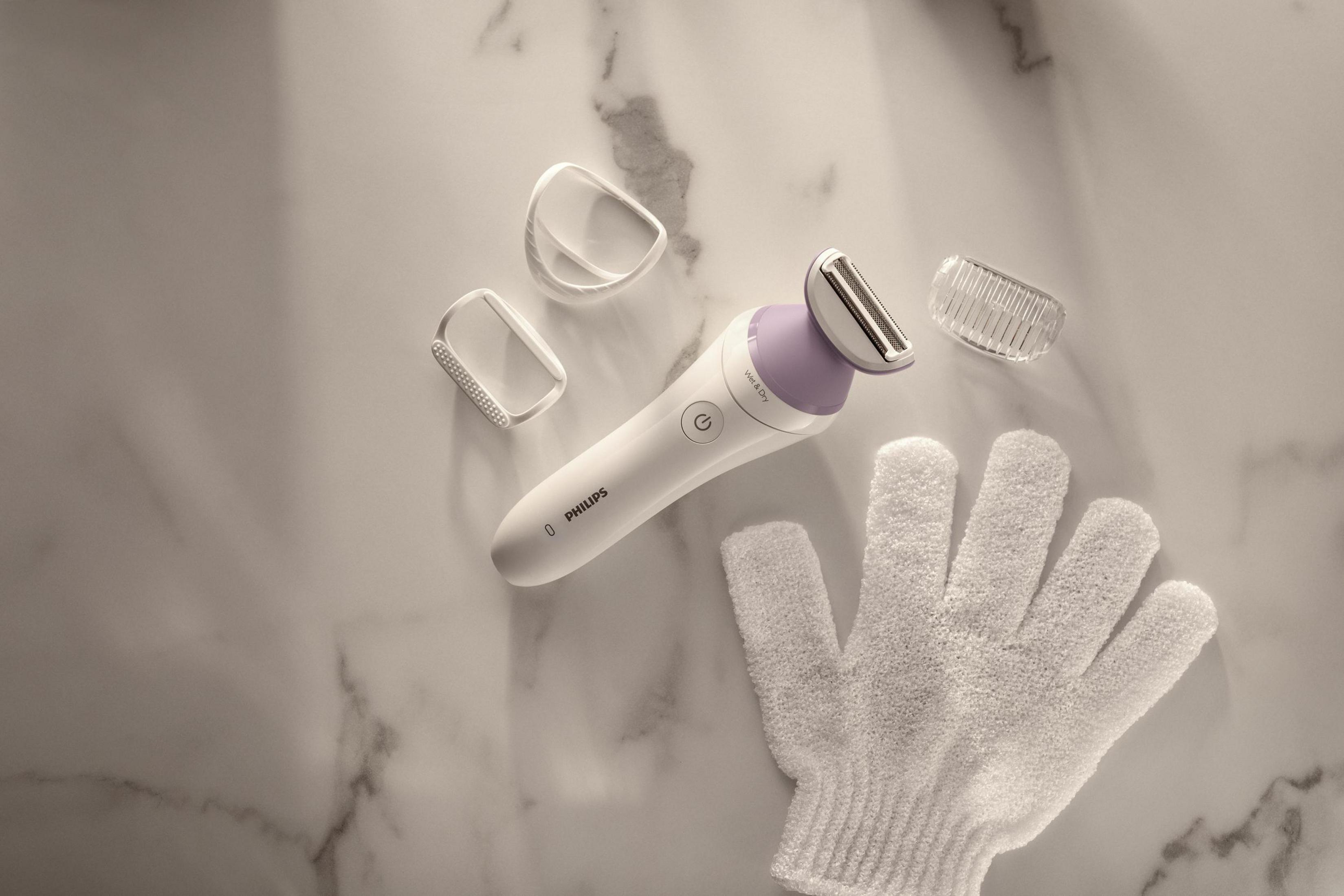 Biała, elektryczna golarka ze akcesoriami. Golarka i akcesoria znajdują się na marmurowym blacie.