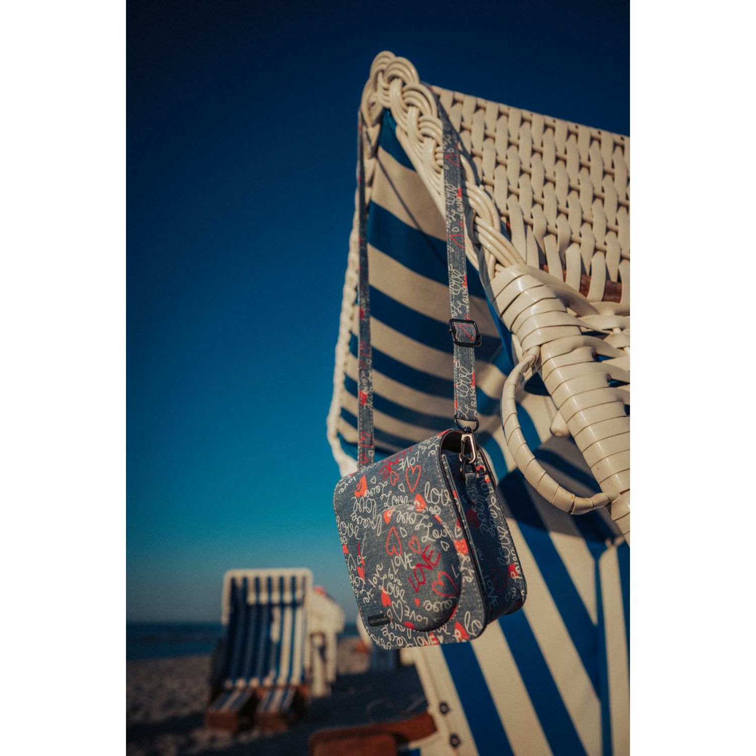 Strandtasche hängt an einem Strandstuhl. Blauer Himmel. Die Tasche hat ein Liebesmuster.